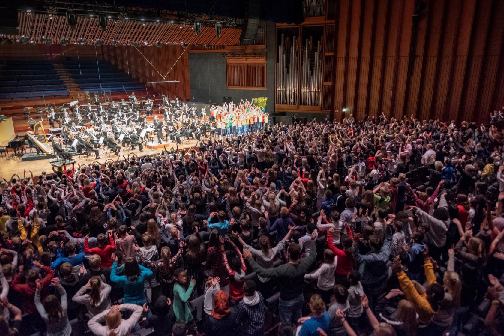 Oslo konserthus med filharmonien på scenen og dansende skolebarn i salen