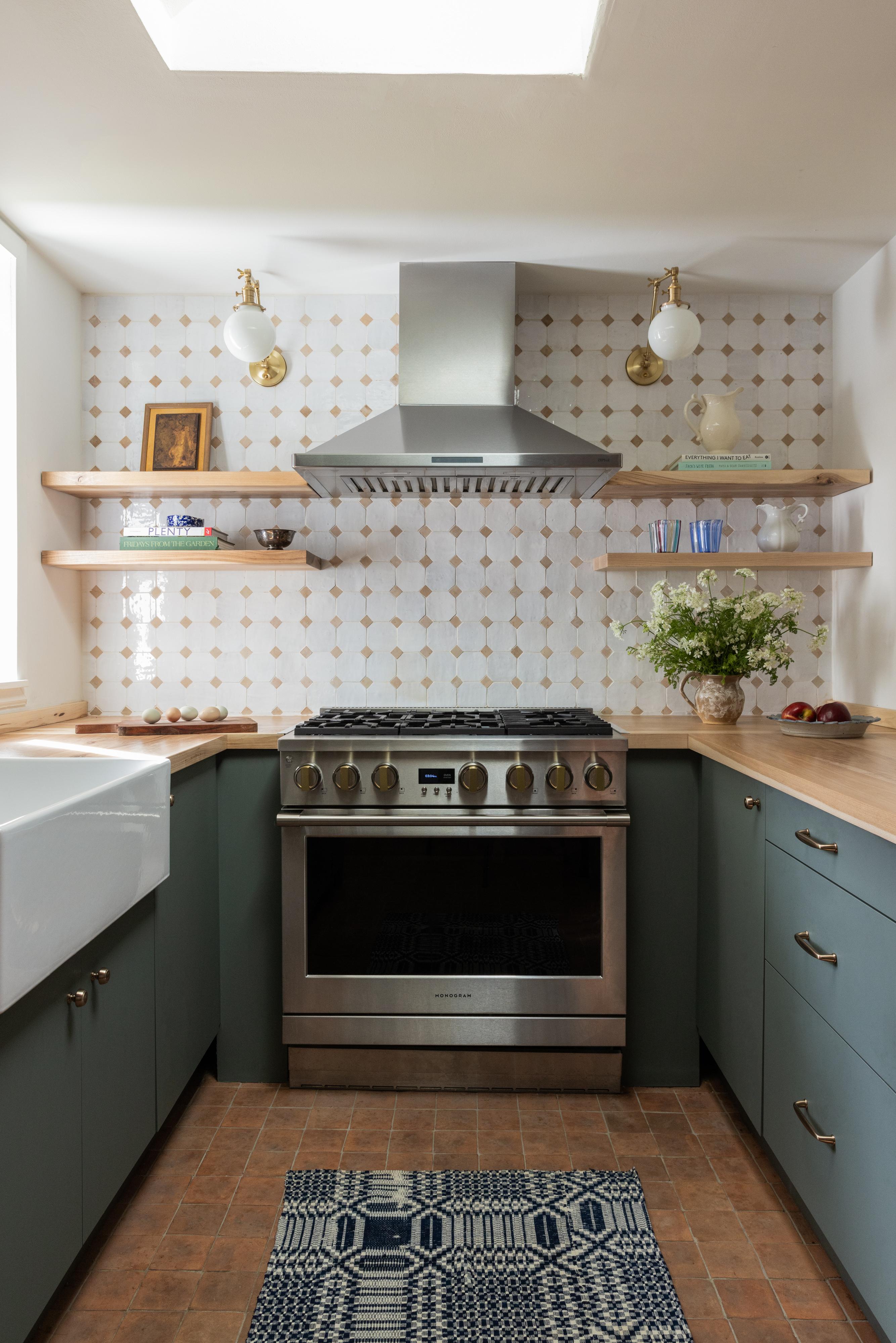 Kitchen range with stainless hood, zellige diamond tile backsplash, paired brass globe sconces, and sage green cabinets designed by Studio VAE.