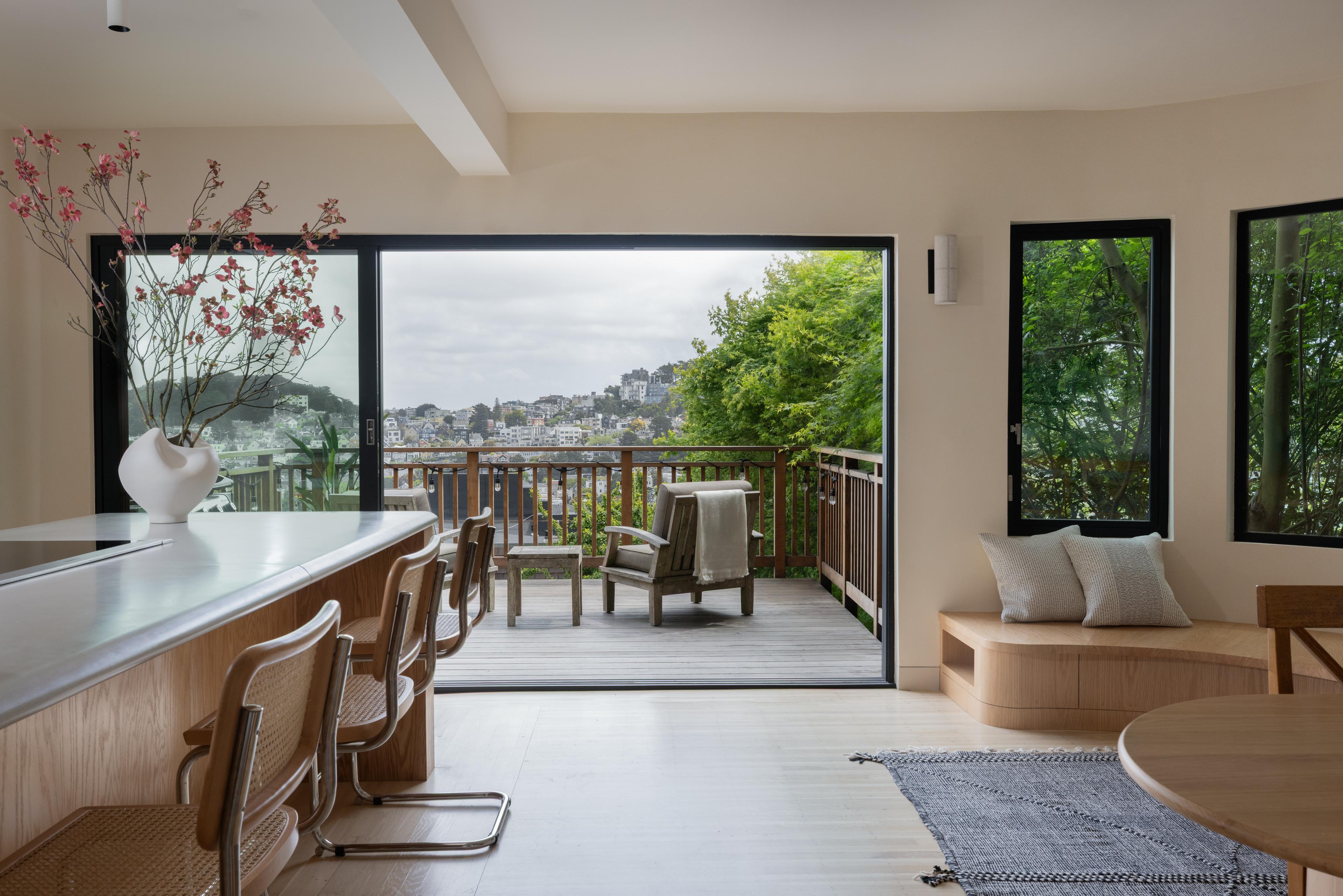 Warm minimalist San Francisco home featuring red oak island, cane cantilever bar stools, opening to a deck with city views