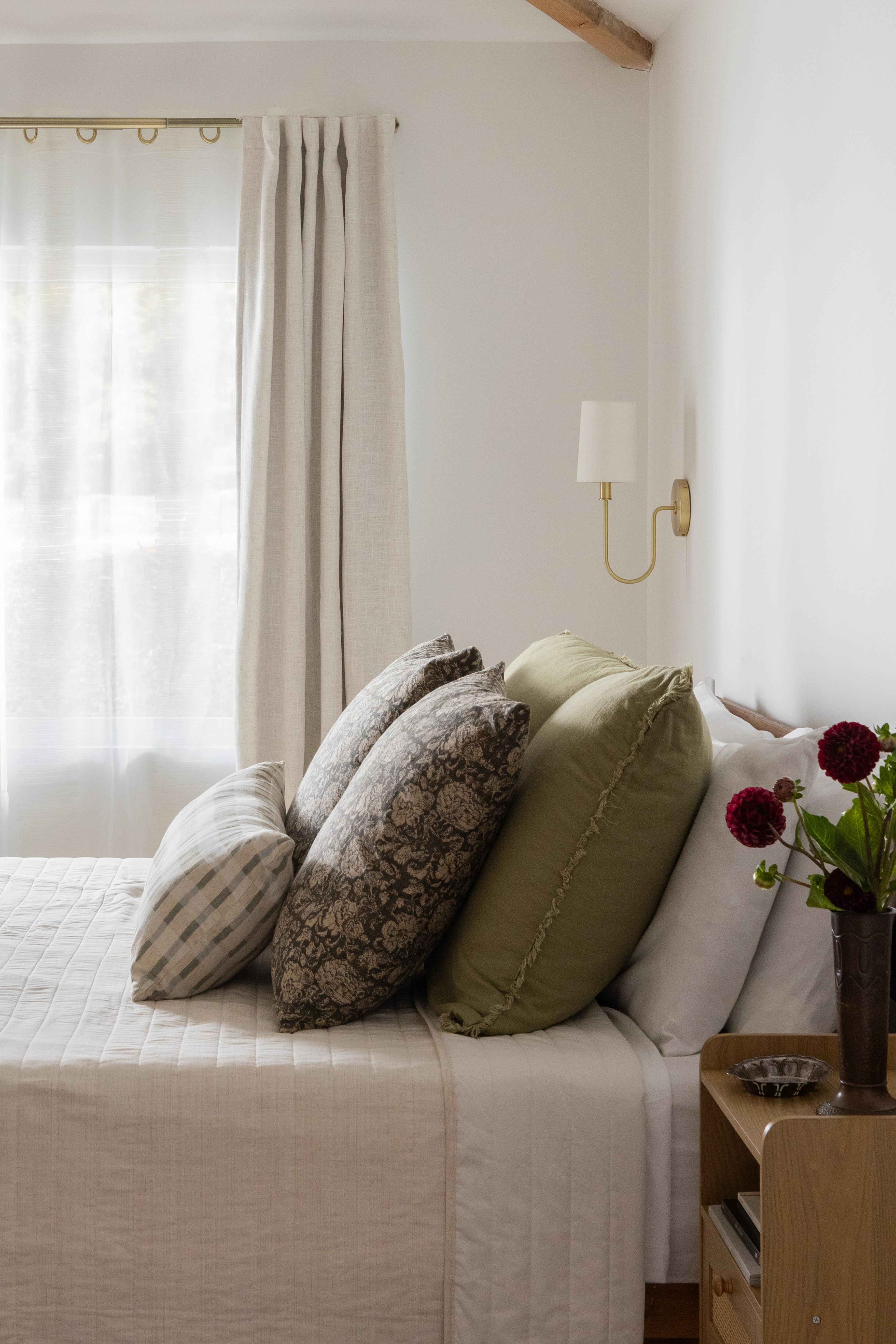 Bedroom bedside detail with layered linen pillows, brass sconce, and dahlia stems in Carmichael home designed by Studio VAE, San Francisco interior designer.
