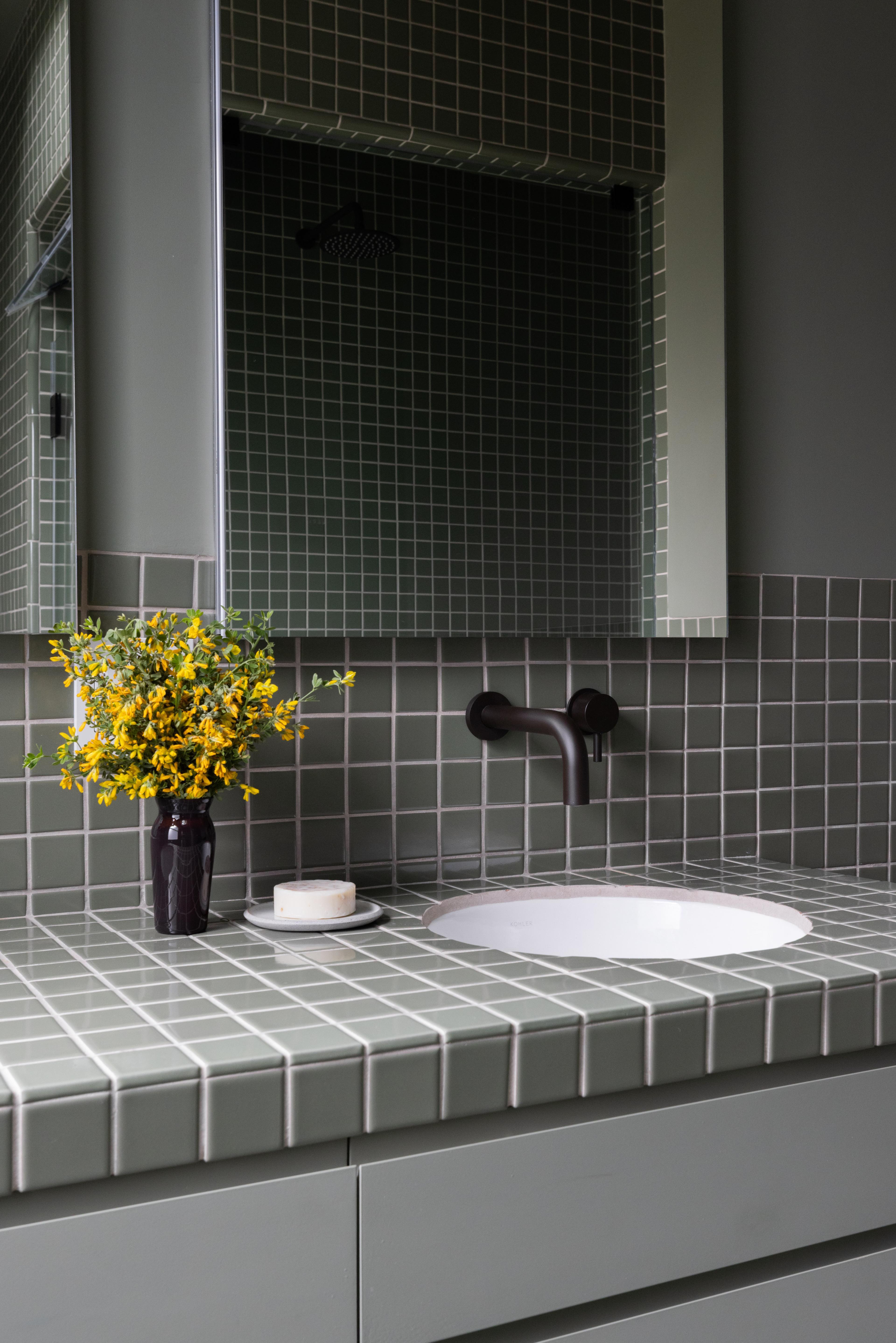 Primary bathroom vanity detail with green tile counter, undermount sink, and yellow flowers in a Studio VAE residential project.
