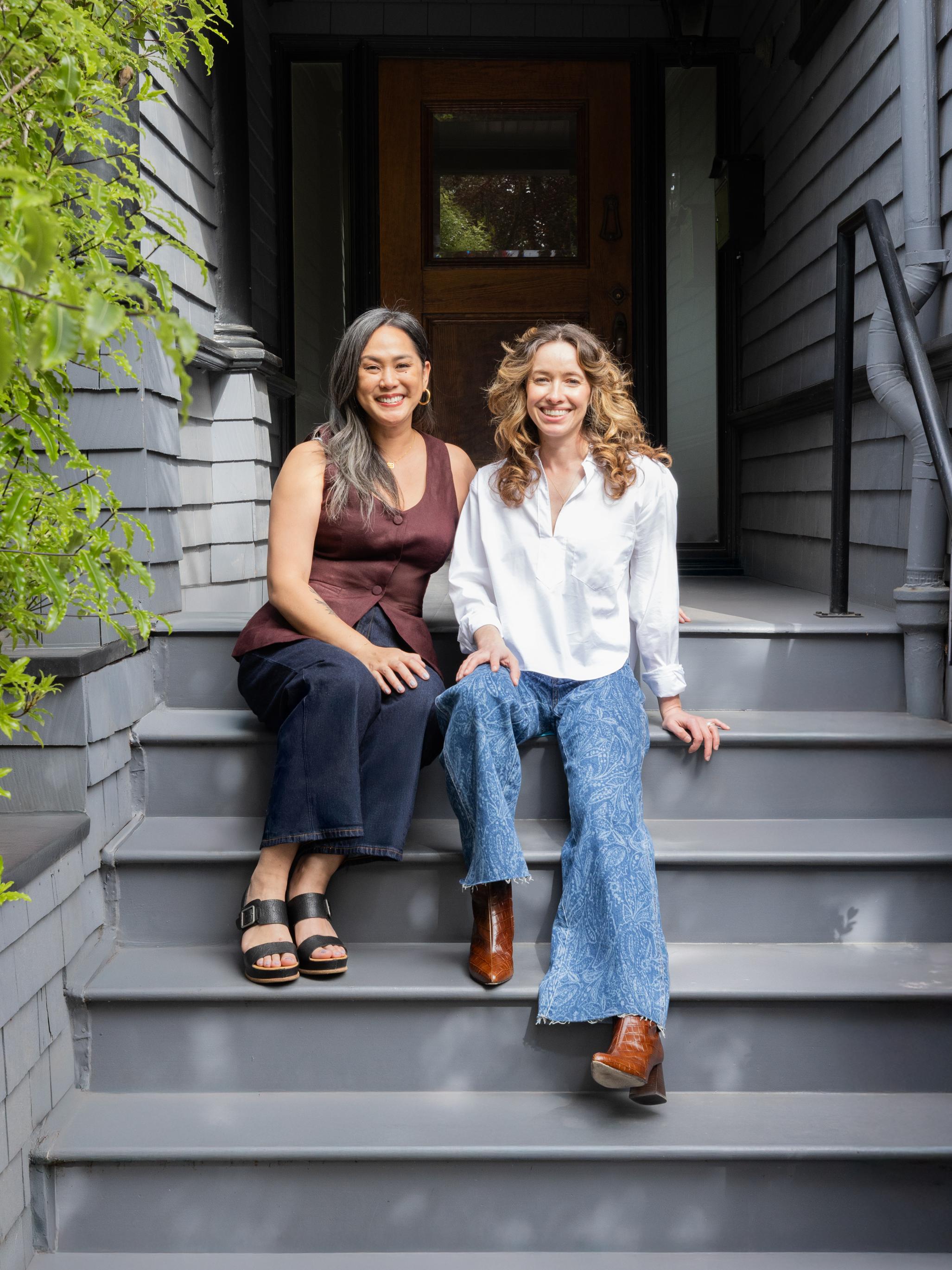 Veronica Jurist and Aggie Revane, principal designers and co-owners of Studio VAE, sitting on the front steps of a house