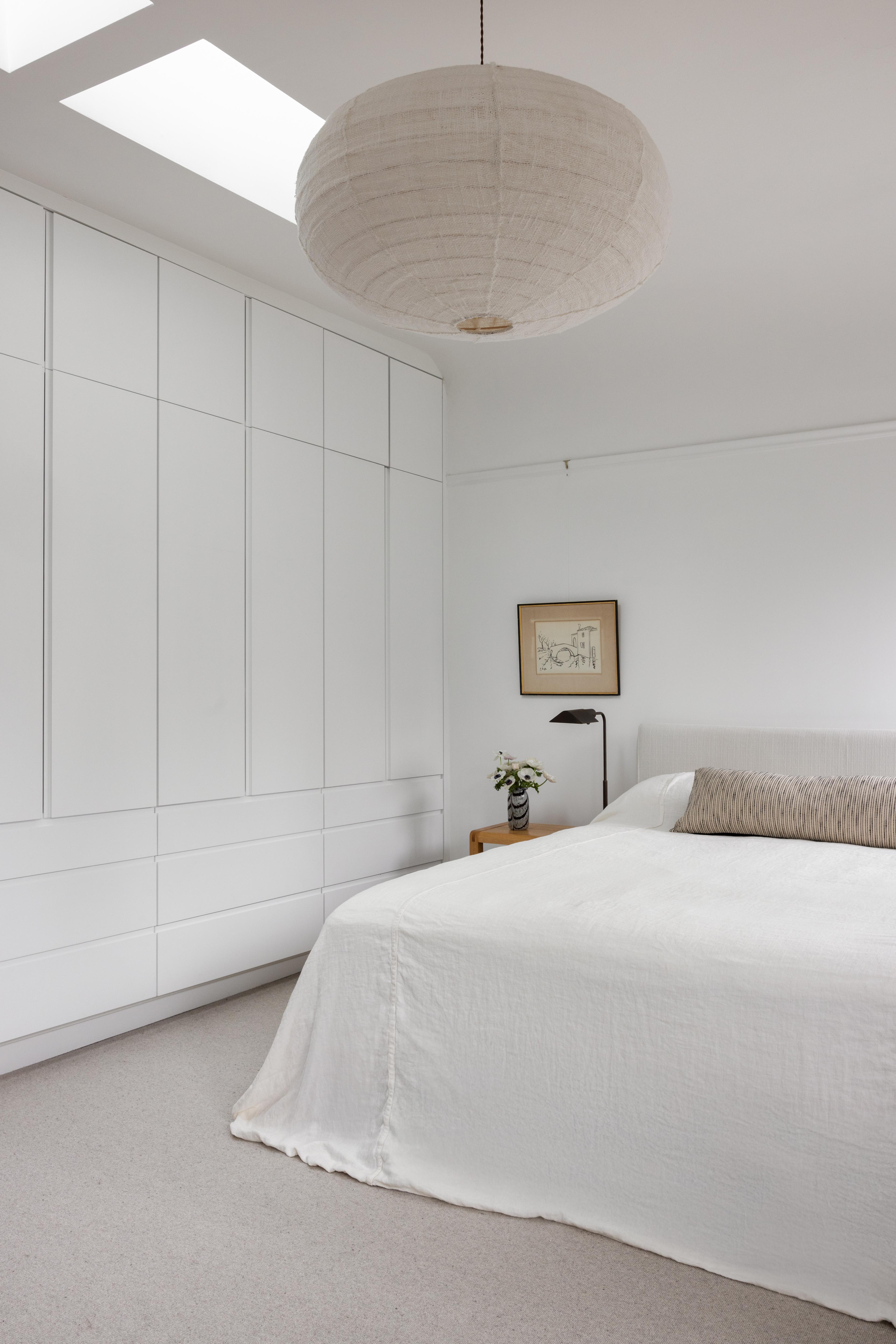 Primary bedroom with floor-to-ceiling white built-in wardrobes, skylight, and paper pendant designed by Studio VAE, San Francisco interior designer.