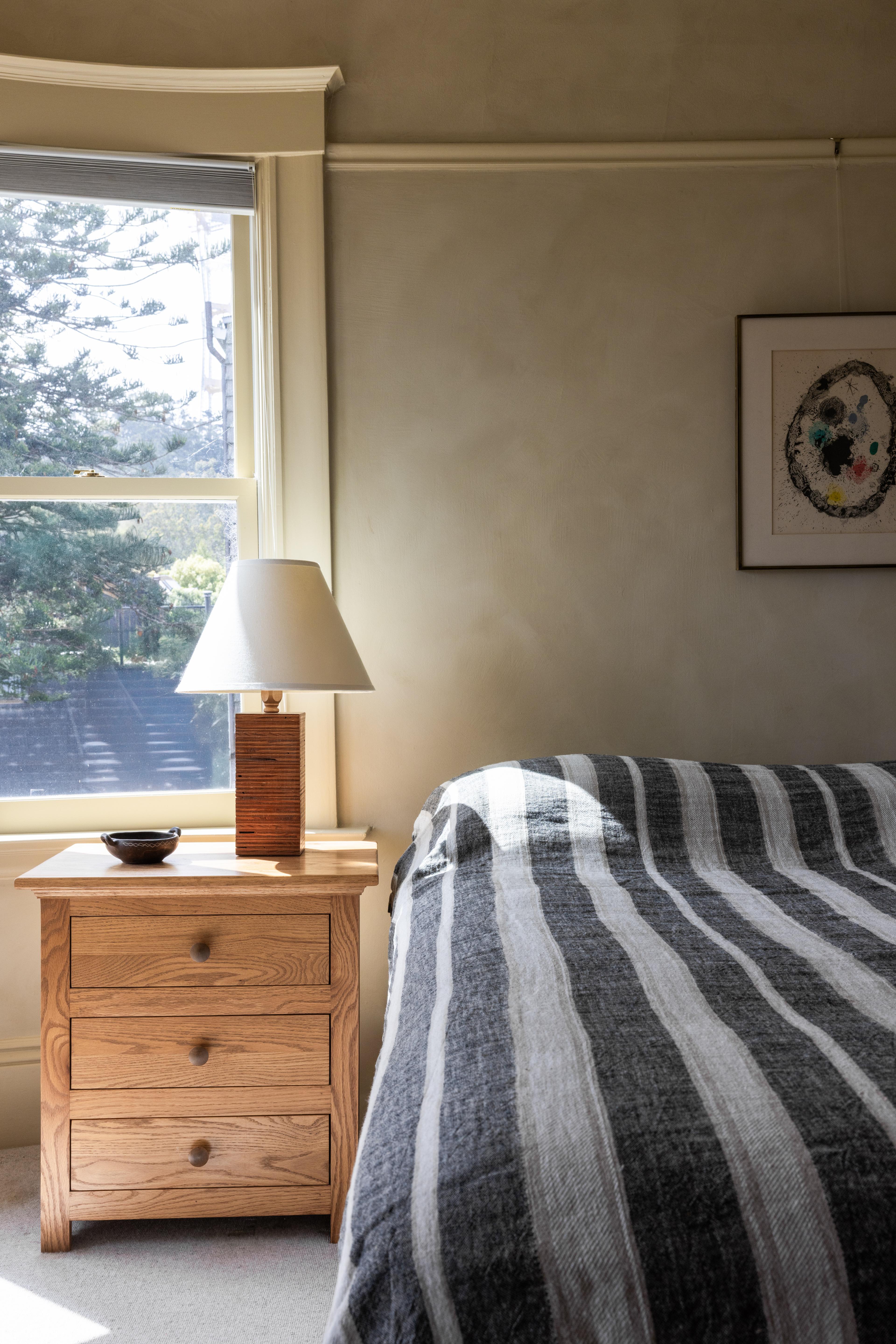 Guest bedroom detail with oak nightstand, table lamp, and framed abstract print in a Studio VAE residential project.