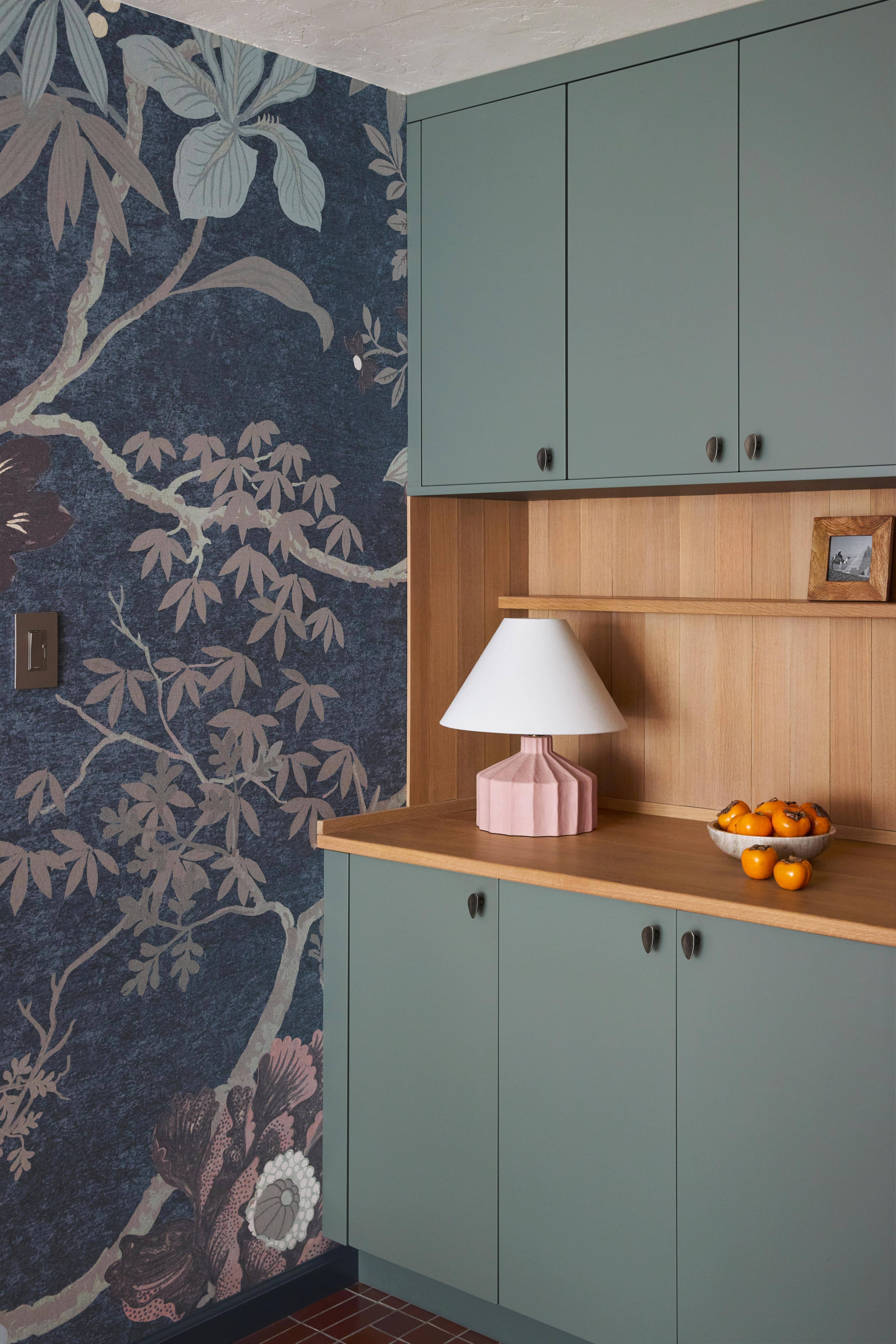 Kitchen with sage green cabinets, oak shelving, pink fluted lamp, and chinoiserie-inspired wallpaper accent wall, designed by Studio VAE.