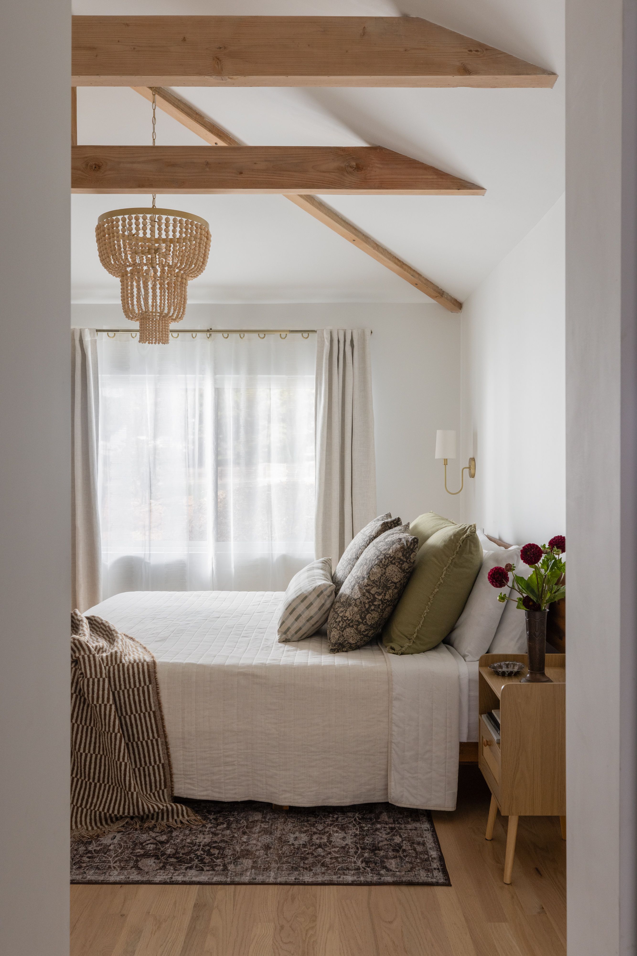 Carmichael bedroom with vaulted ceiling and exposed wood beams, beaded pendant light, linen bedding, and a vintage rug