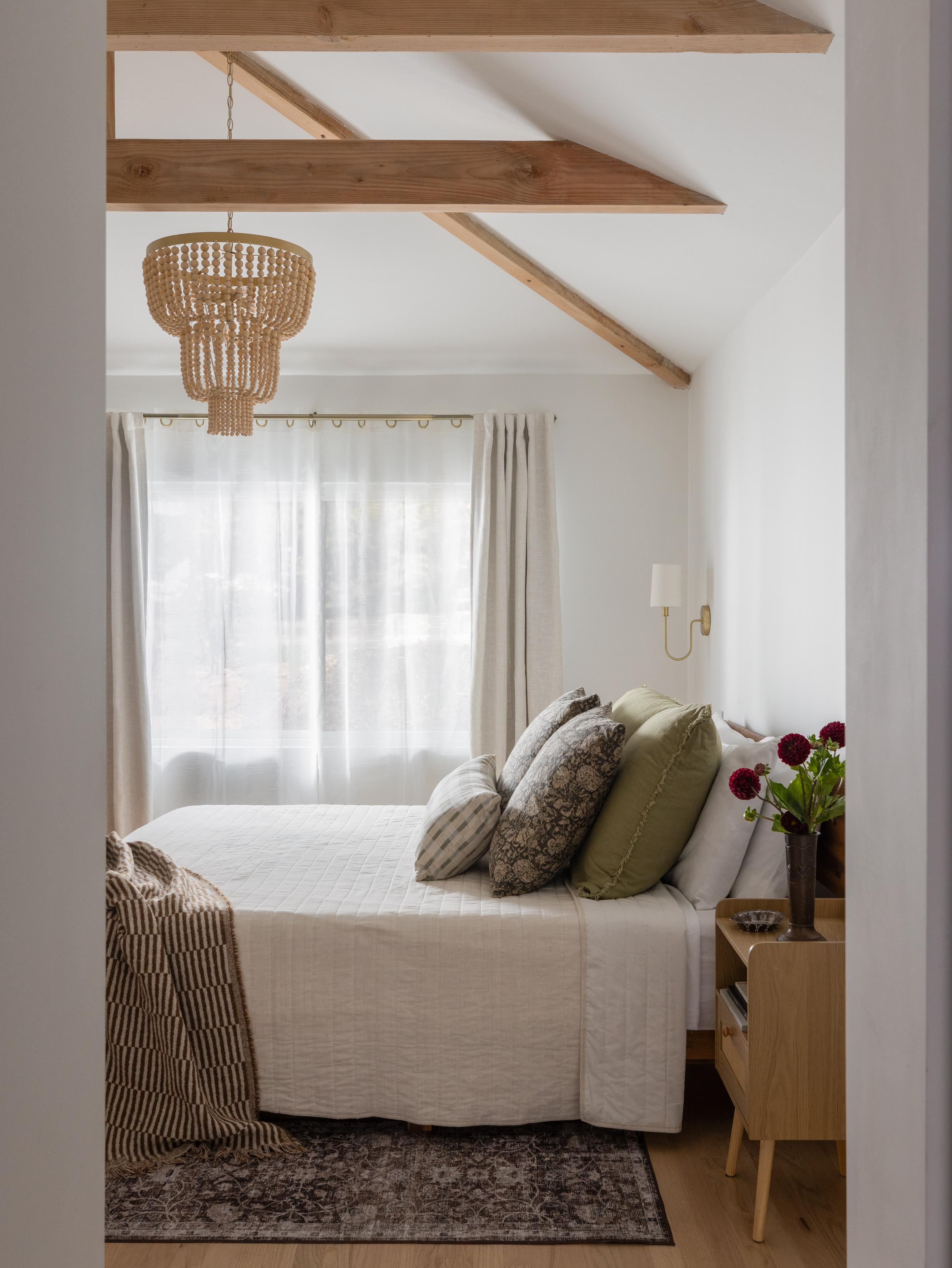 Carmichael bedroom with vaulted ceiling and exposed wood beams, beaded pendant light, linen bedding, and a vintage rug