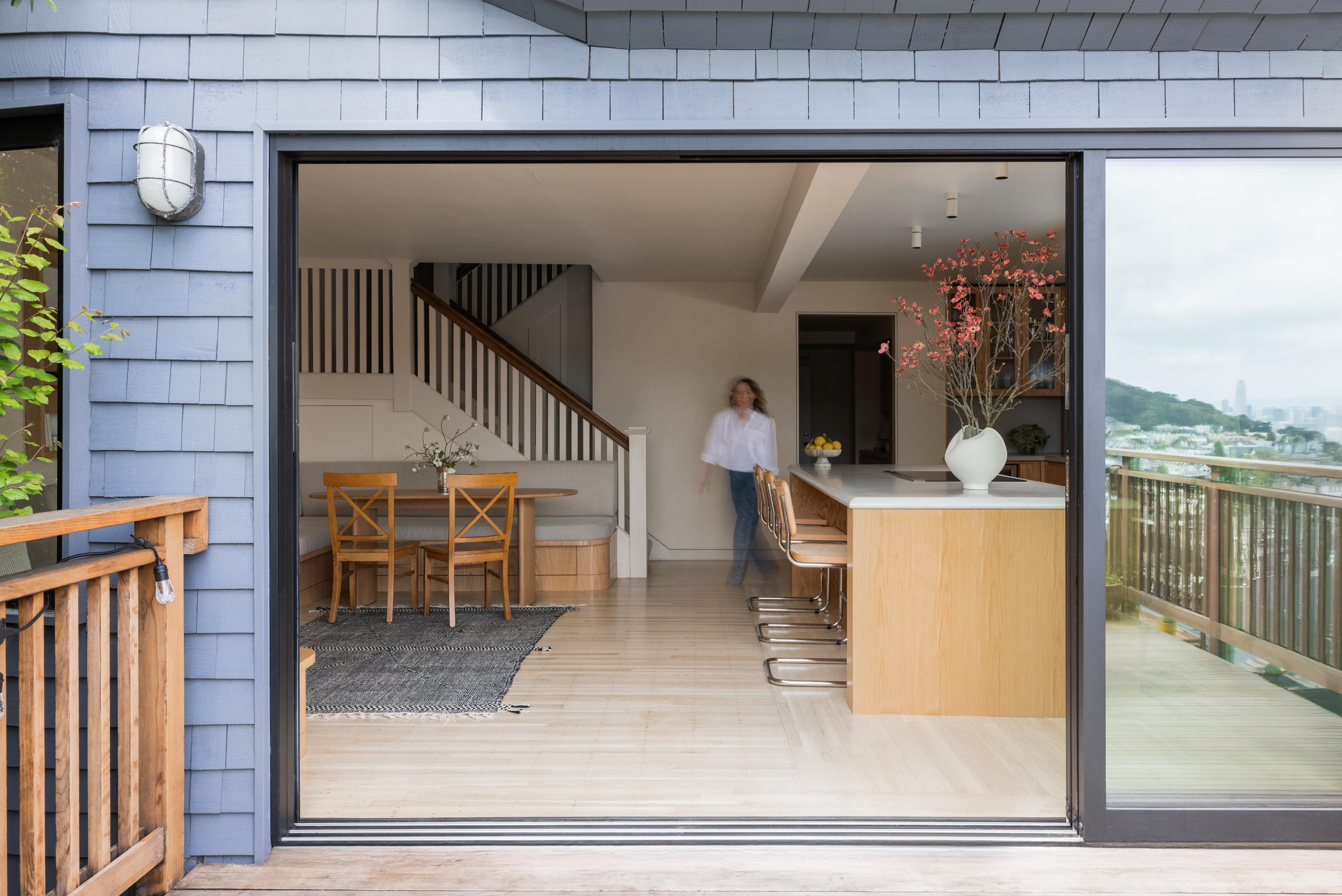 Parnassus Heights kitchen and dining area seen from the deck through open sliding doors, with an oak island and cane counter stools, designed by Studio VAE