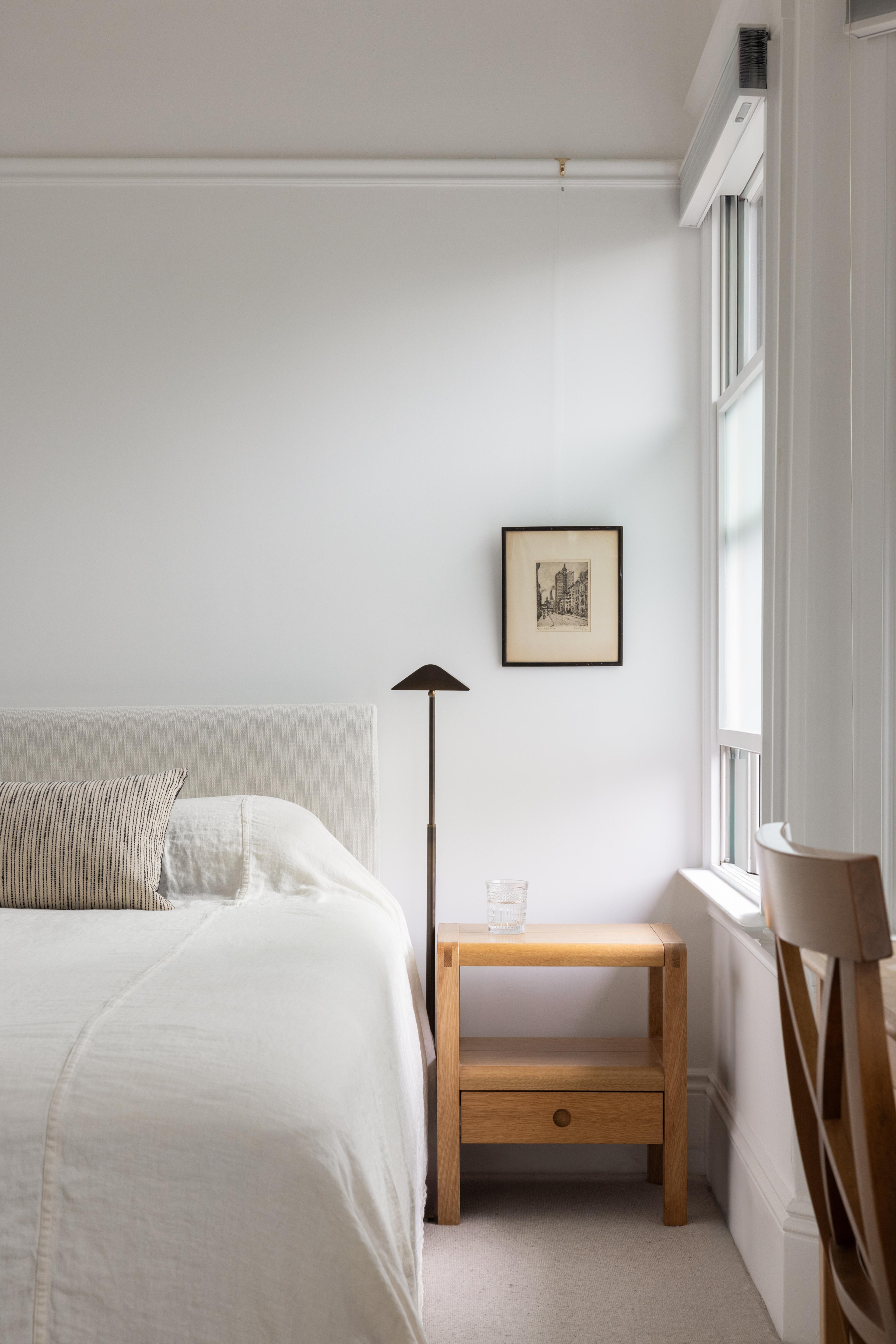 Primary bedroom with cream upholstered headboard, oak block nightstand, and framed pen-and-ink drawing in Parnassus Heights home designed by Studio VAE.