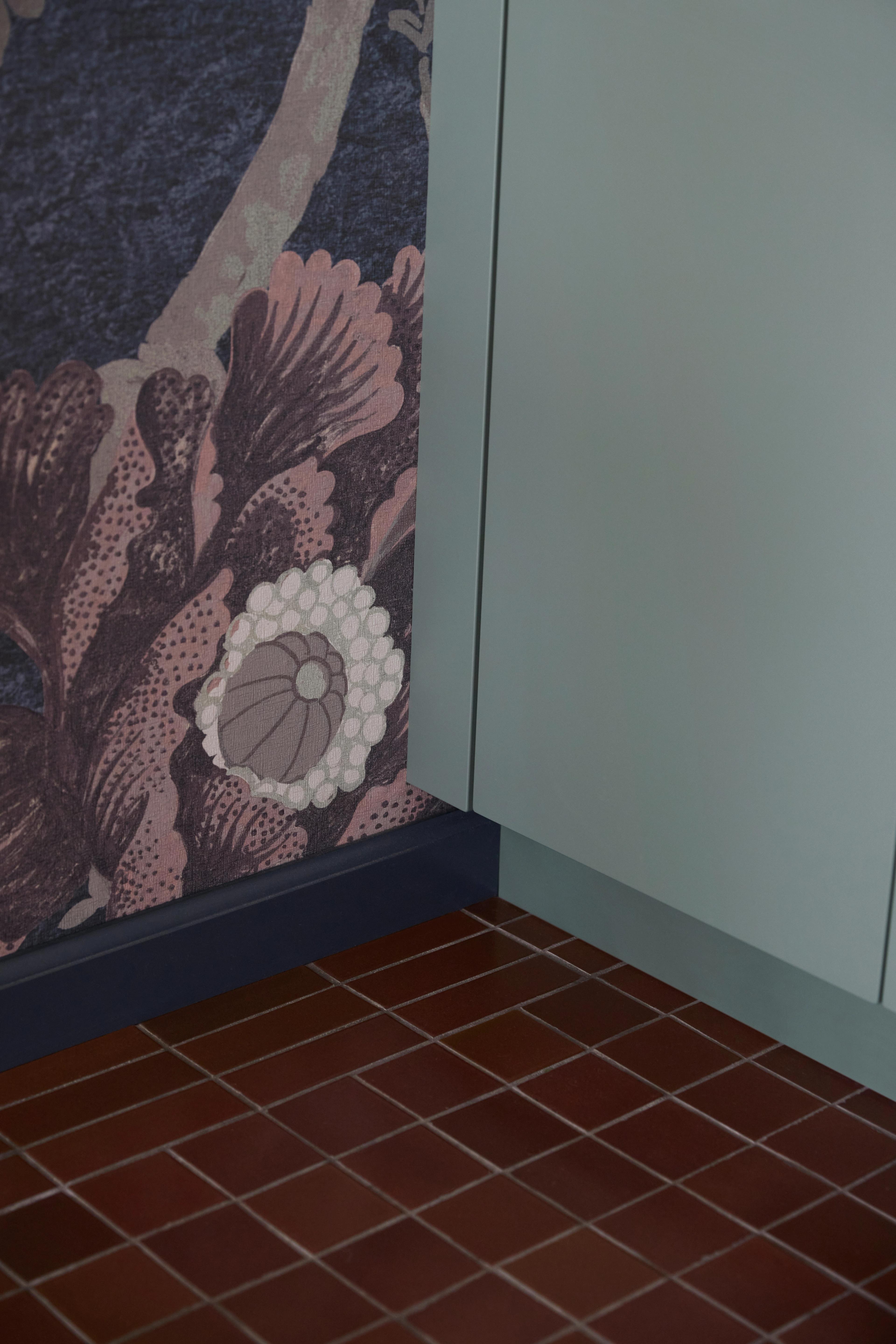 Kitchen detail showing terracotta tile floor meeting chinoiserie-inspired wallpaper and sage green cabinets, designed by Studio VAE.