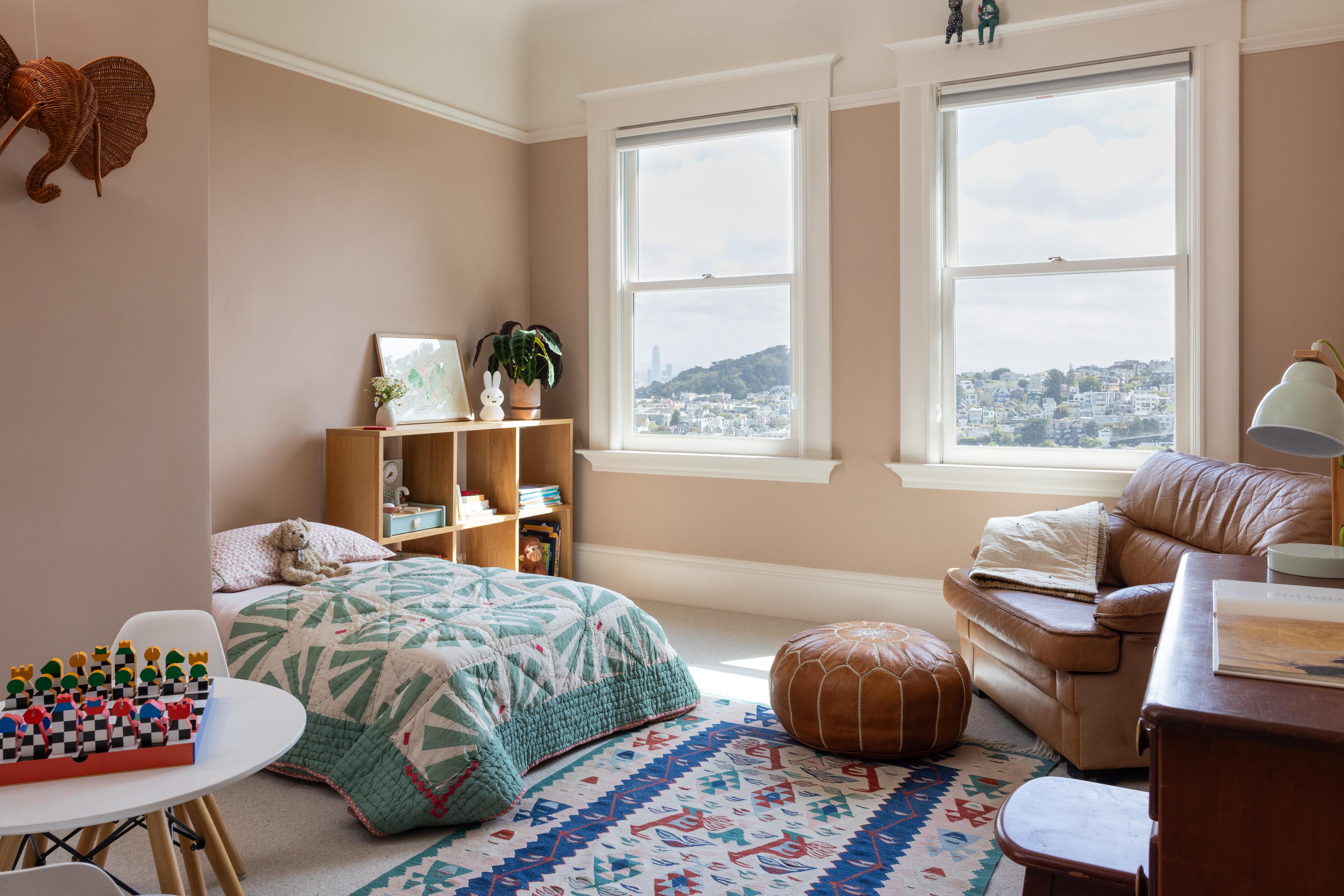 Children’s bedroom with blush walls, vintage rug, and twin bed beneath windows overlooking the San Francisco skyline, in Parnassus Heights home designed by Studio VAE.