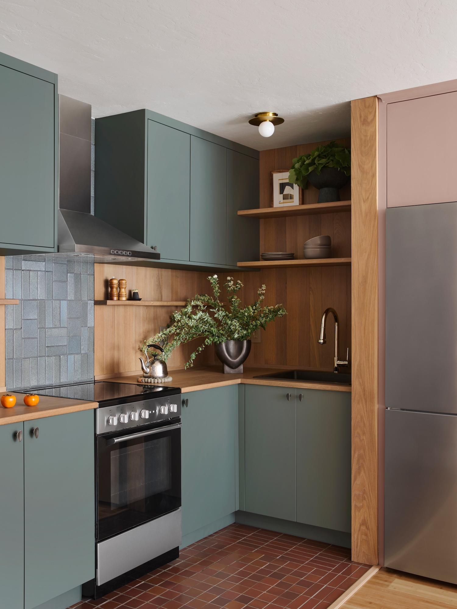 Outer Sunset kitchen with sage green cabinets, white oak countertops and shelves, a blue Heath tile backsplash, and terracotta floor tile, designed by Studio VAE