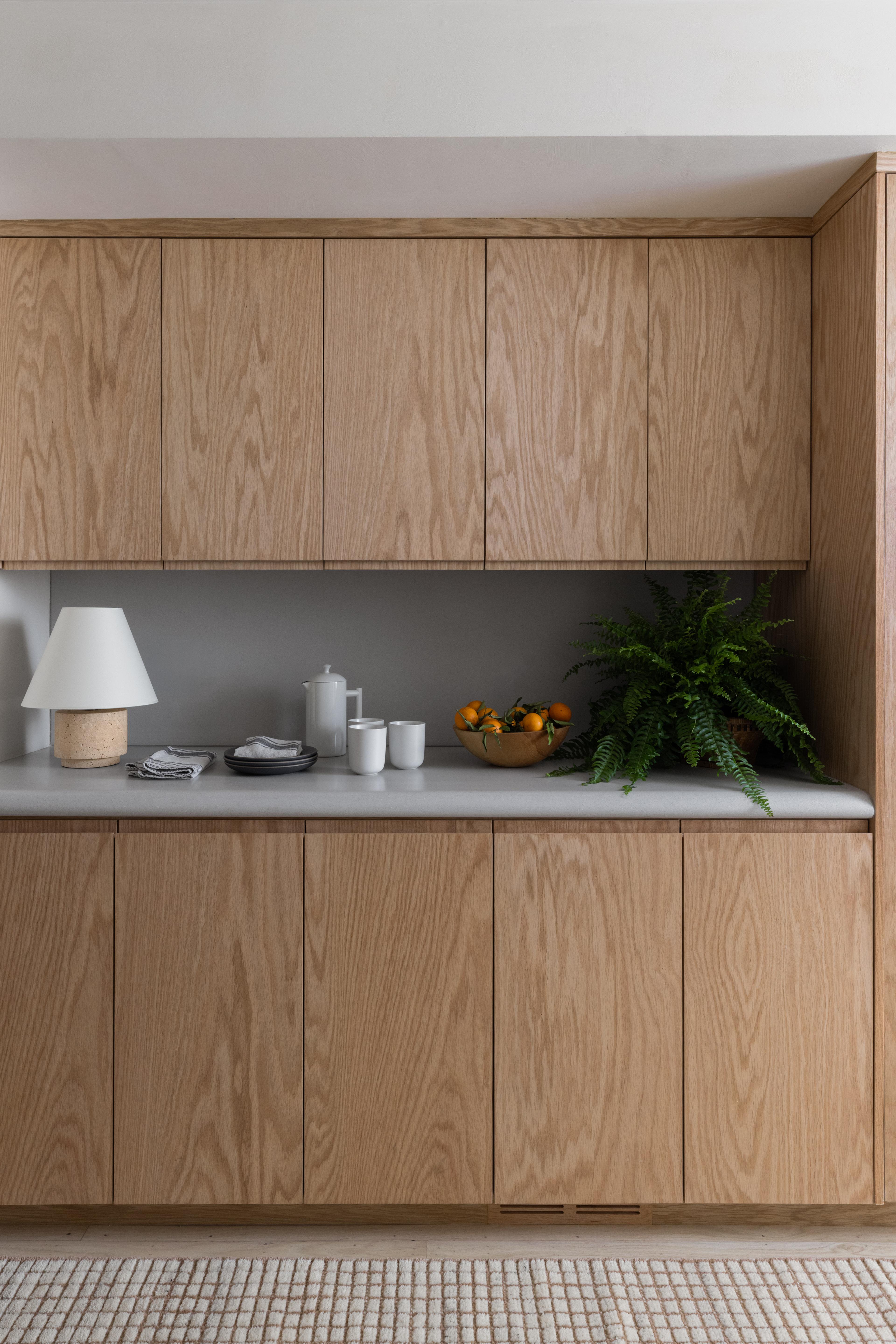 Custom red oak built-in cabinetry styled as a coffee station with travertine lamp and Boston fern, designed by Studio VAE, San Francisco interior designer.