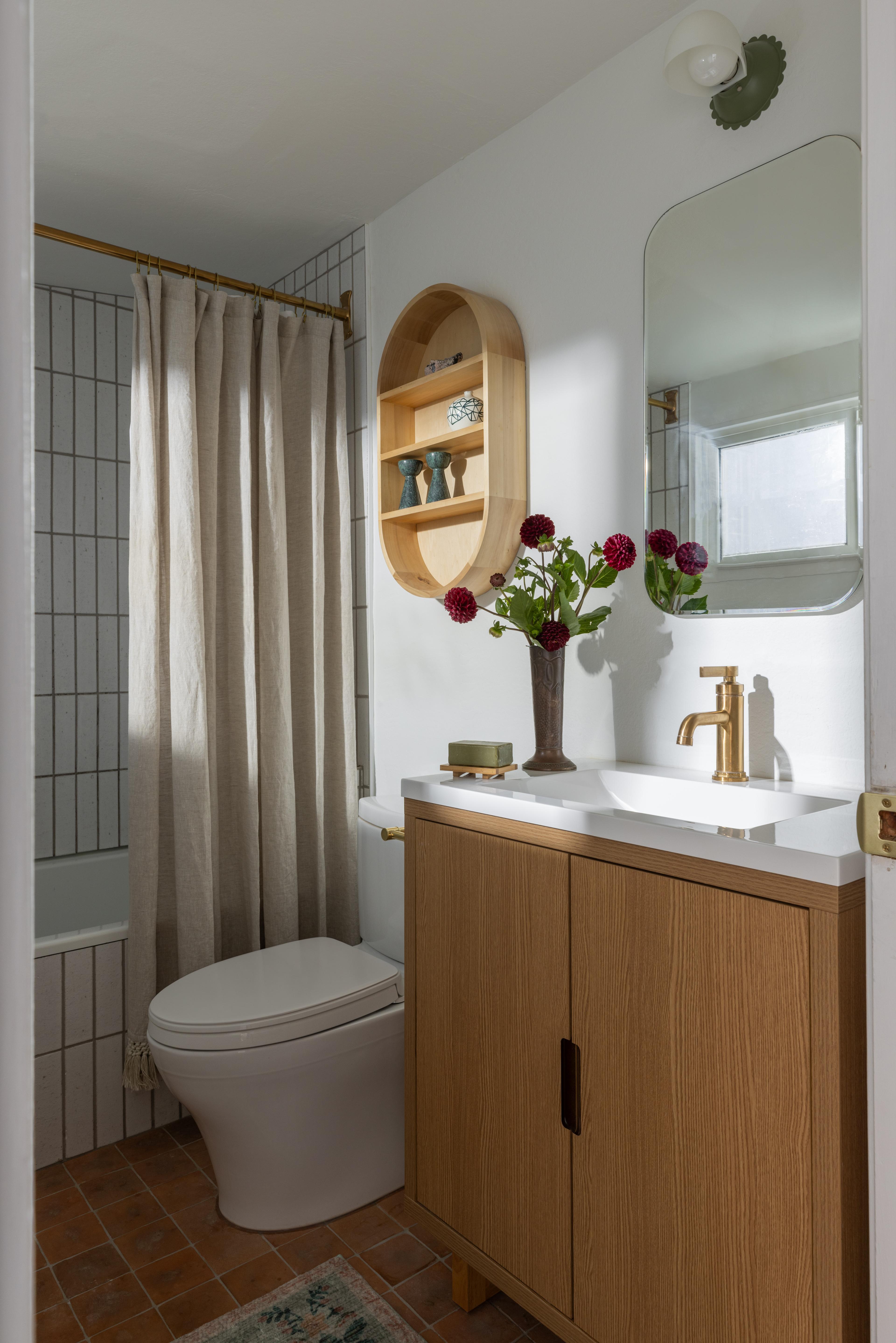 Bathroom with white oak vanity, brushed brass faucet, oval wood wall shelf, and dahlias in Carmichael home designed by Studio VAE, San Francisco interior designer.