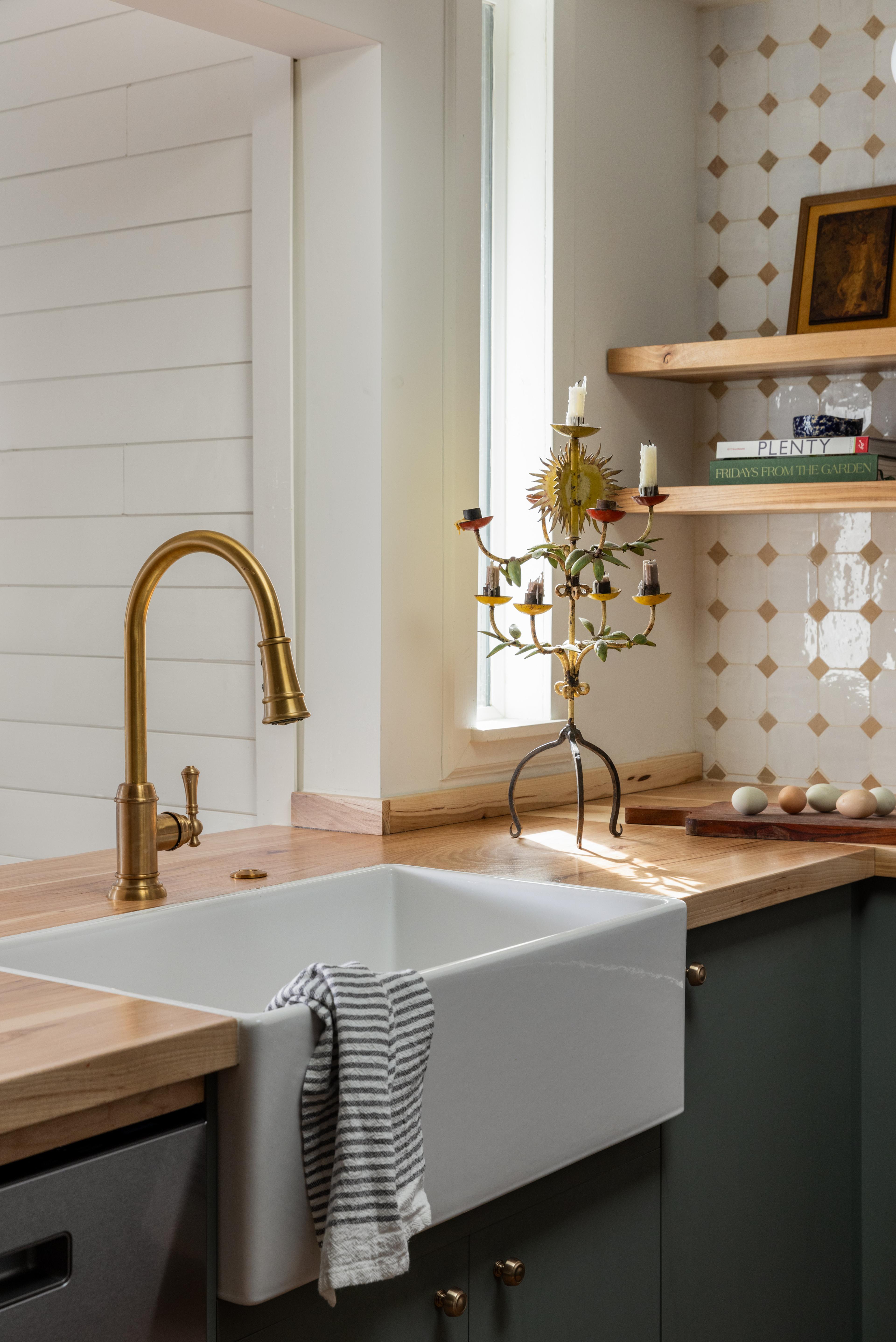 Kitchen with white farmhouse apron sink, brushed brass faucet, sage green cabinets, and hickory countertop designed by Studio VAE.