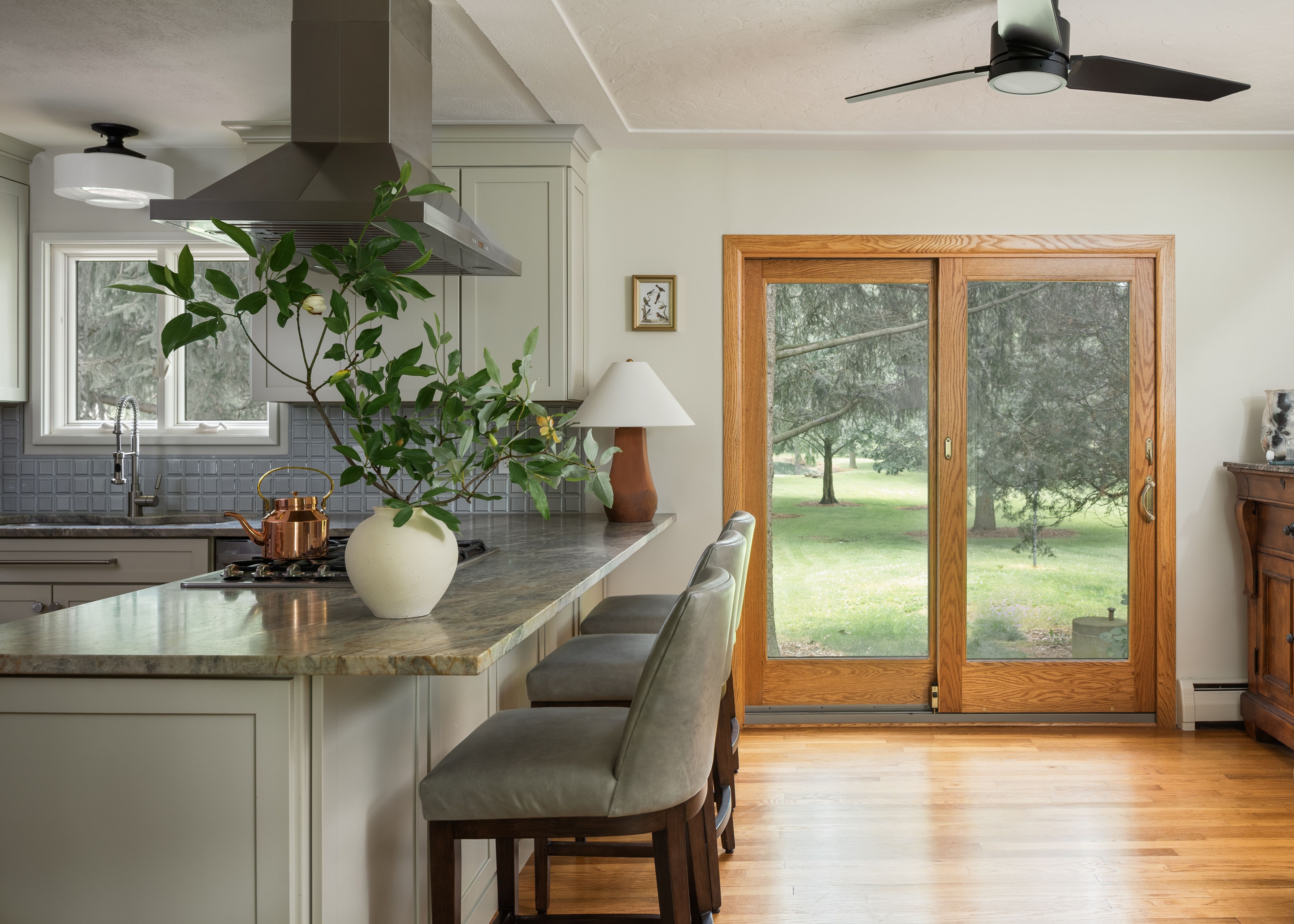 Lorain farmhouse kitchen with a leathered quartzite peninsula, green leather counter stools, and cream Shaker cabinets, designed by Studio VAE