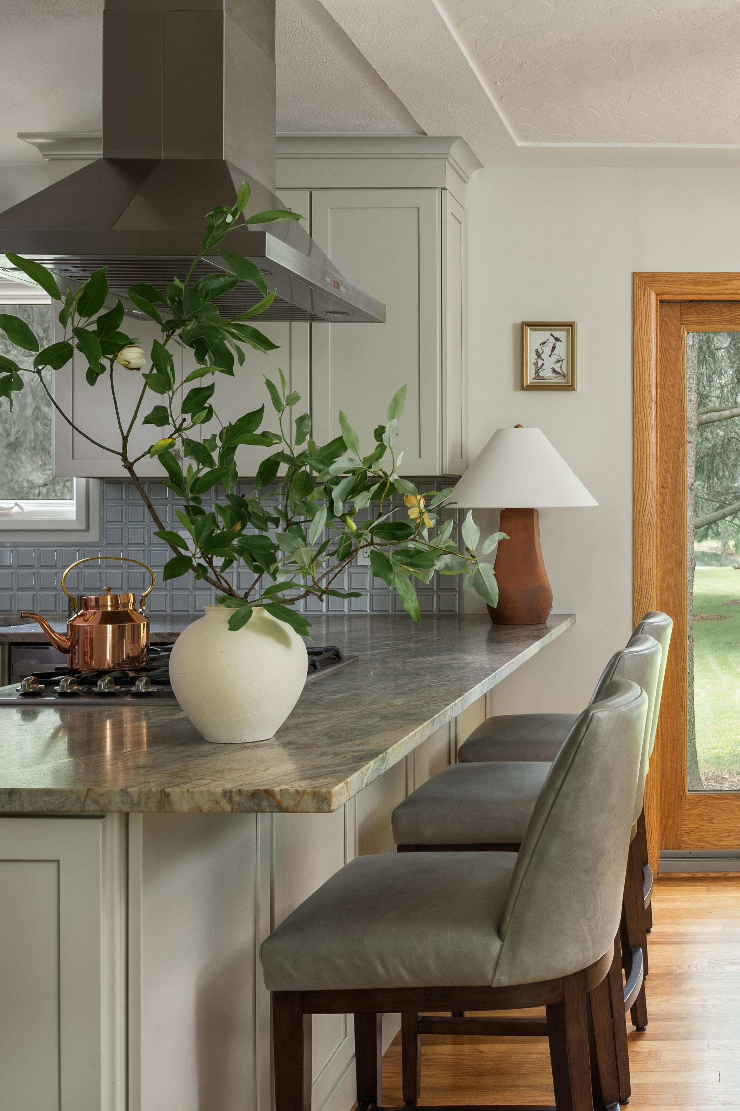 Lorain farmhouse kitchen with a leathered quartzite peninsula, green leather counter stools, and cream Shaker cabinets, designed by Studio VAE