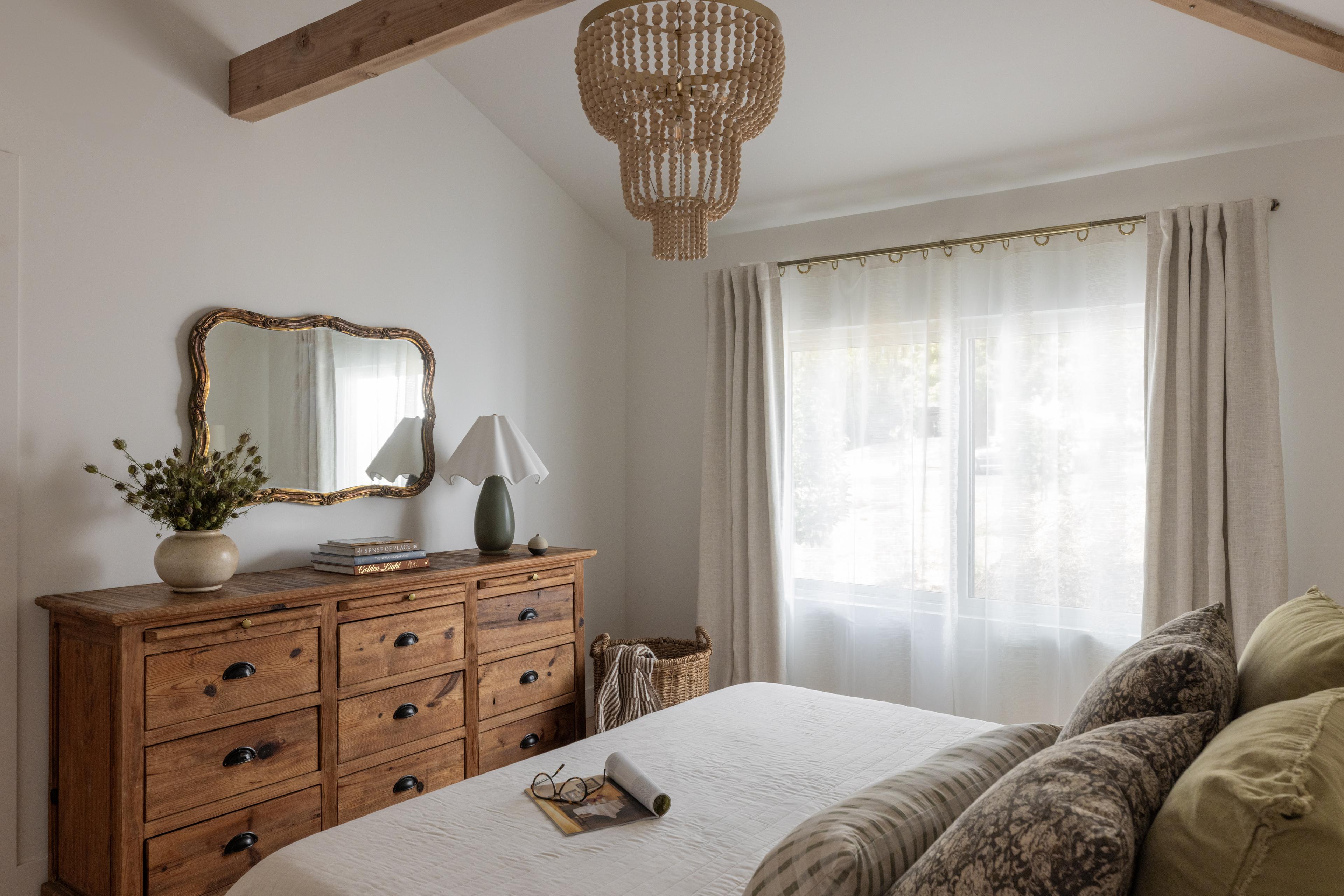 Bedroom with rustic pine dresser, ornate gilt mirror, wood-bead chandelier, and exposed wood beams designed by Studio VAE.