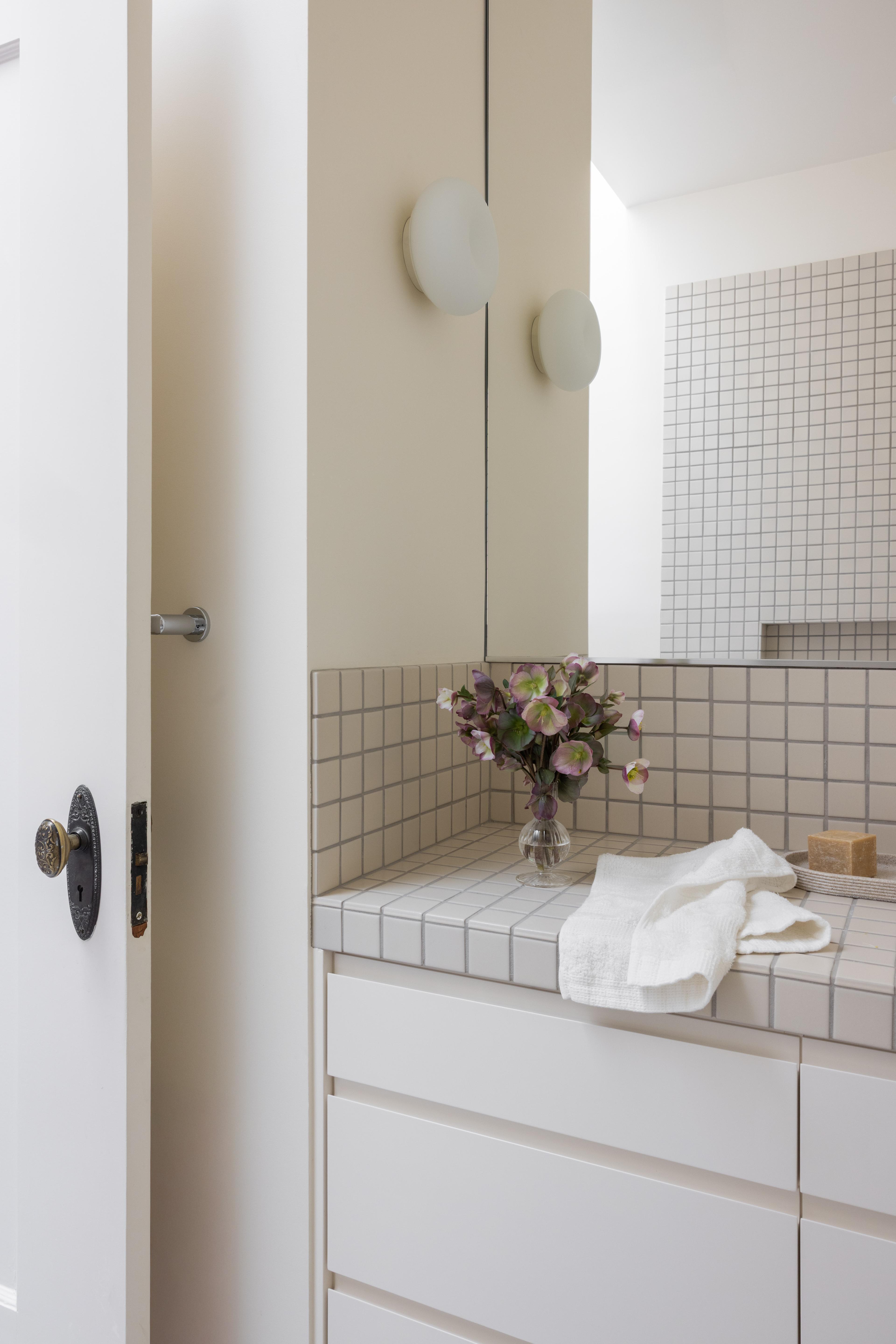 Bathroom vanity with tiled countertop, round vessel sink, and hellebore stems in Parnassus Heights home designed by Studio VAE.