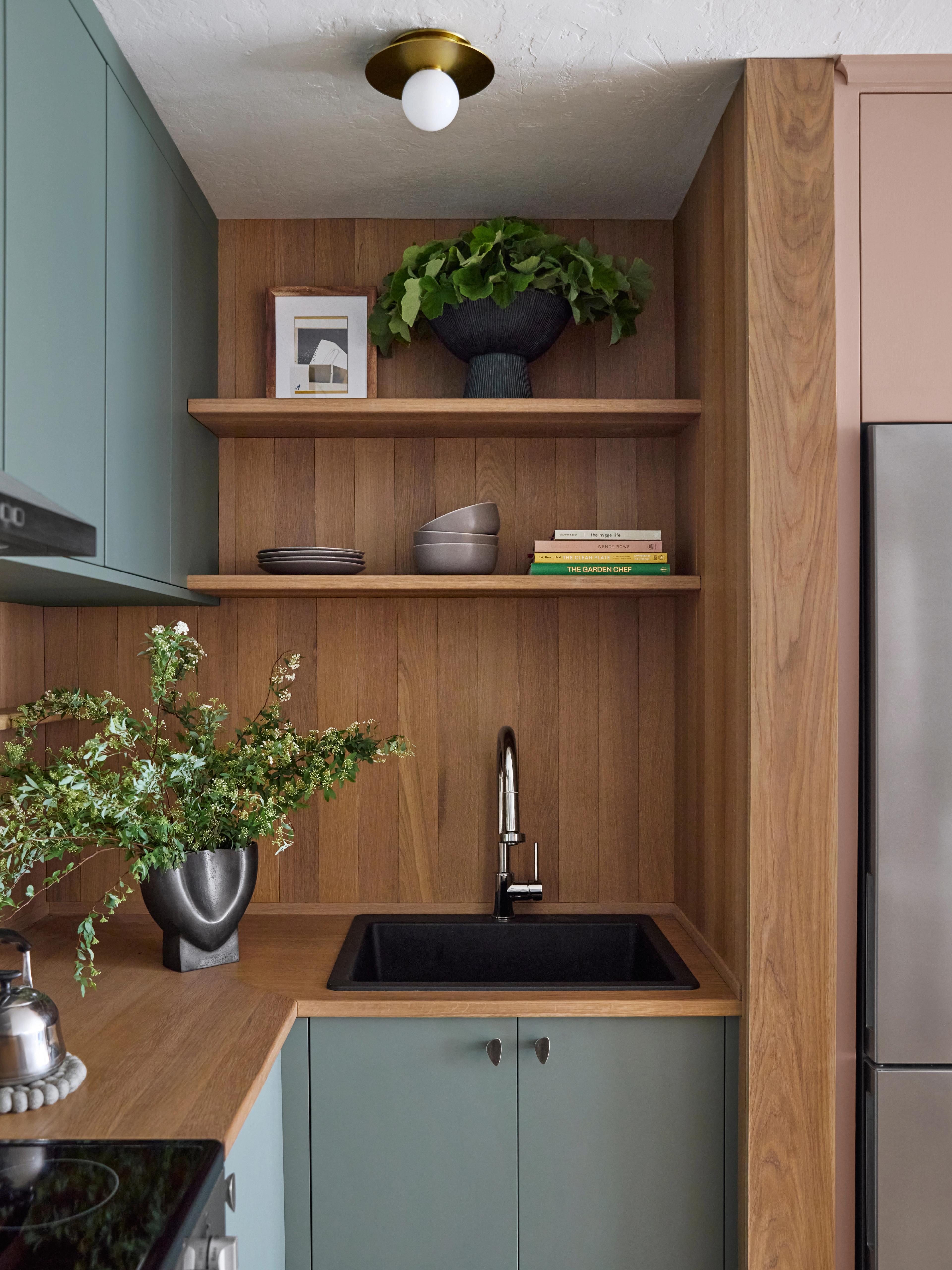 Kitchen corner with white oak open shelving and surround, sage green cabinets, wood plank counter, and black sink, designed by Studio VAE.
