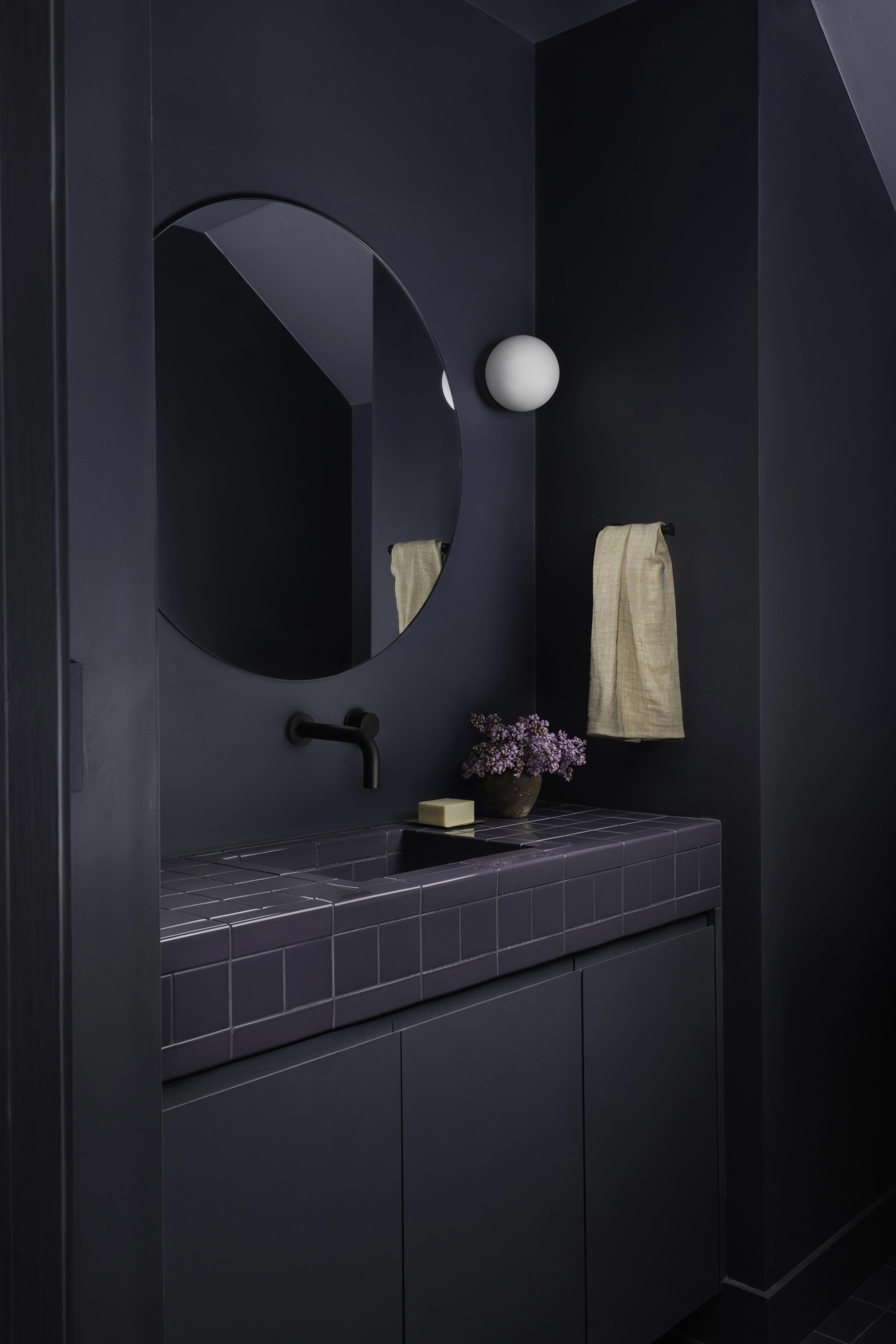 Powder room clad in moody blue paint with tile vanity, round mirror, and globe sconce in Parnassus Heights home designed by Studio VAE.