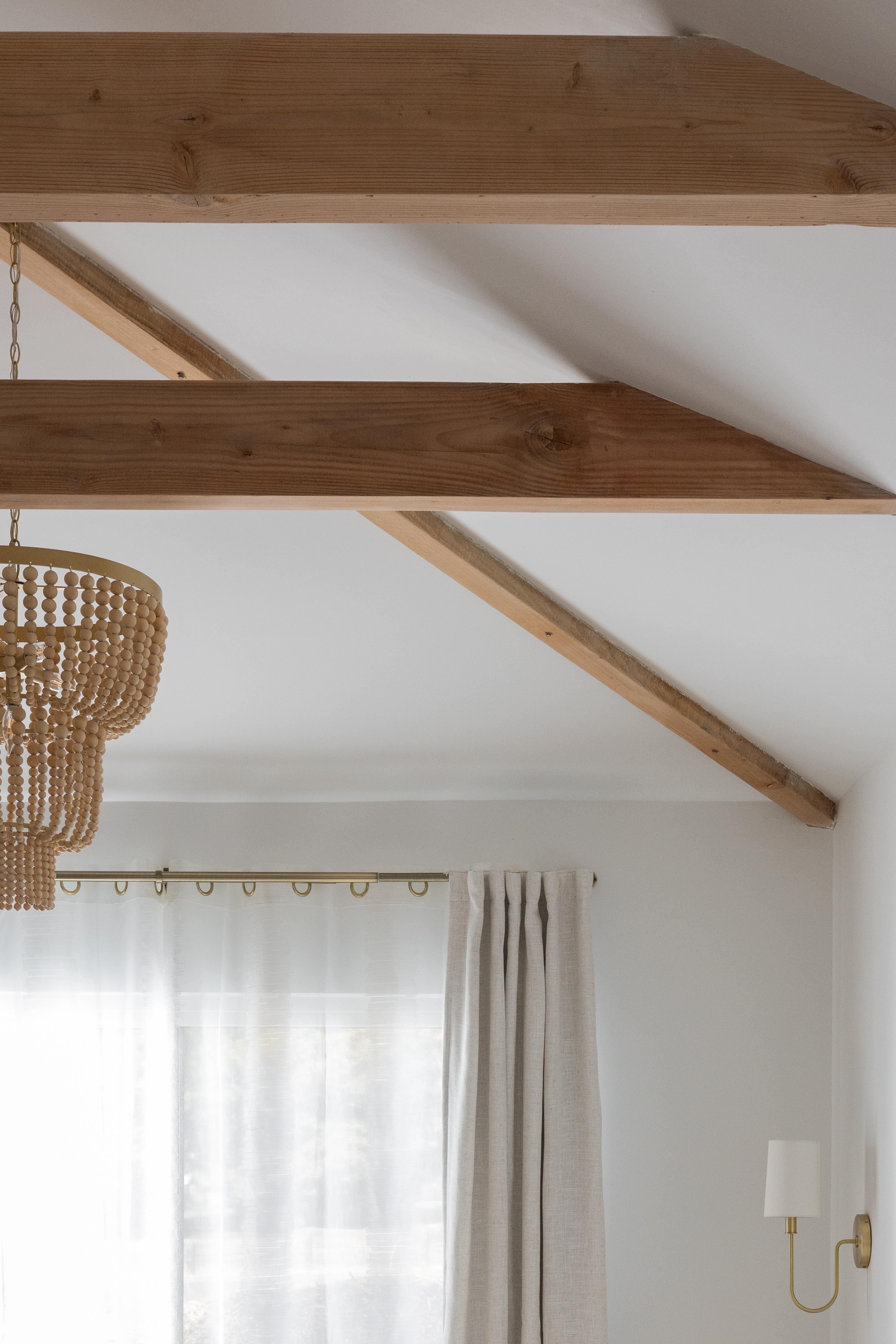 Detail of exposed wood ceiling beams and brass curtain rod in Carmichael bedroom designed by Studio VAE.