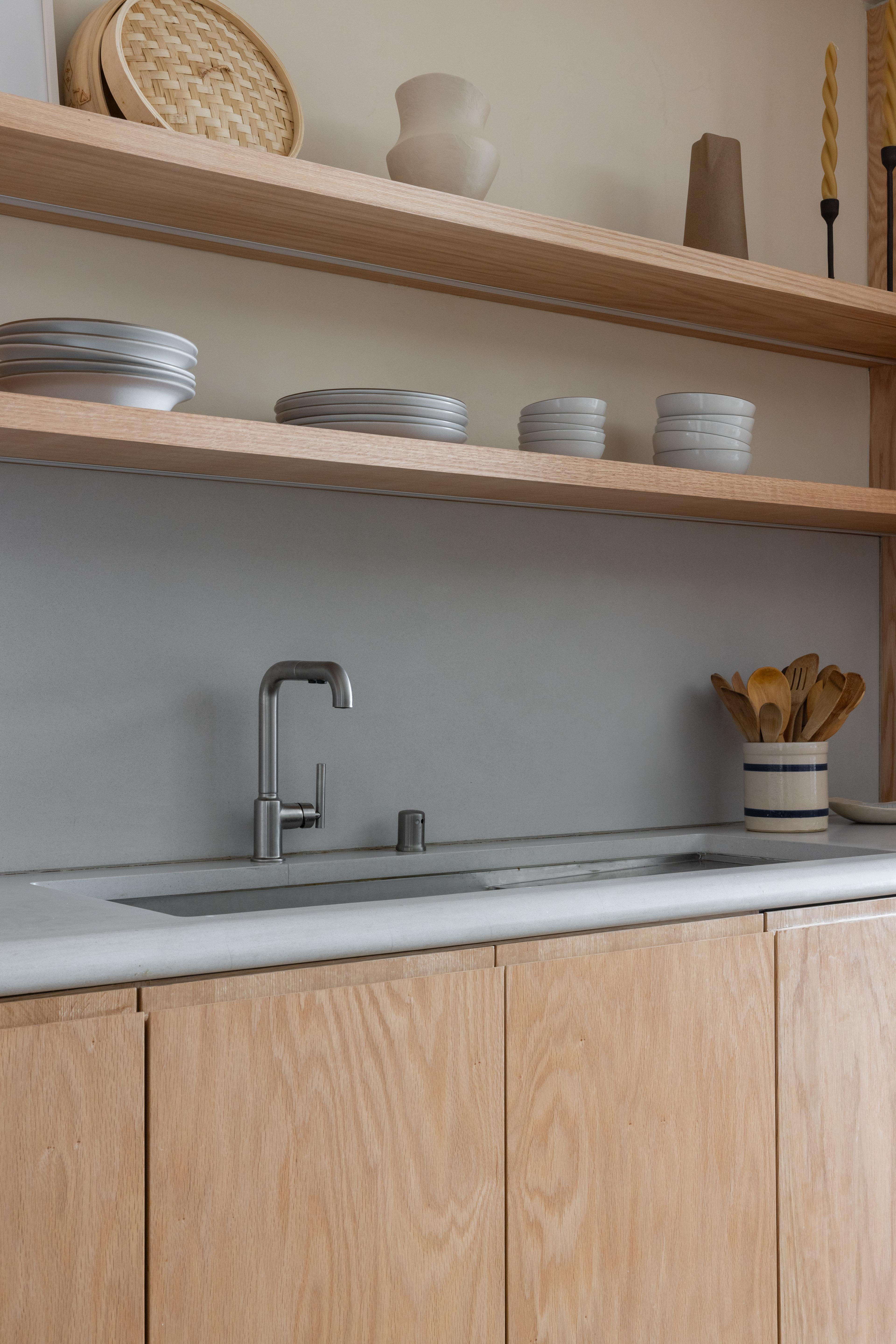 Kitchen sink detail with concrete countertop and brushed nickel fixtures beneath open red oak shelving in Parnassus Heights home designed by Studio VAE.