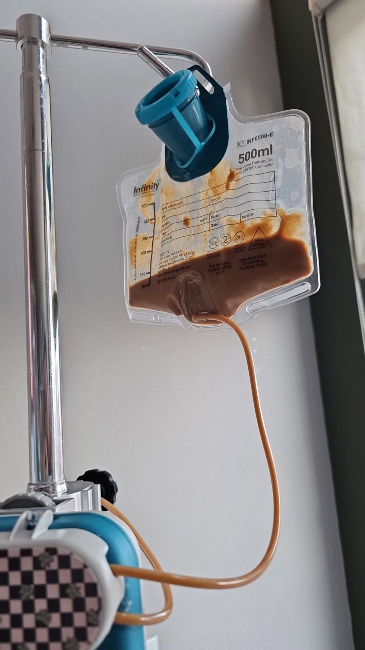 Enteral feeding bag hanging from an IV pole with tubing connected for a home feeding routine.