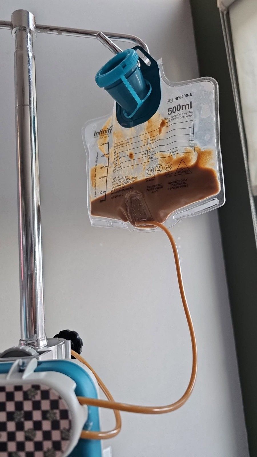 Enteral feeding bag hanging from an IV pole with tubing connected for a home feeding routine.