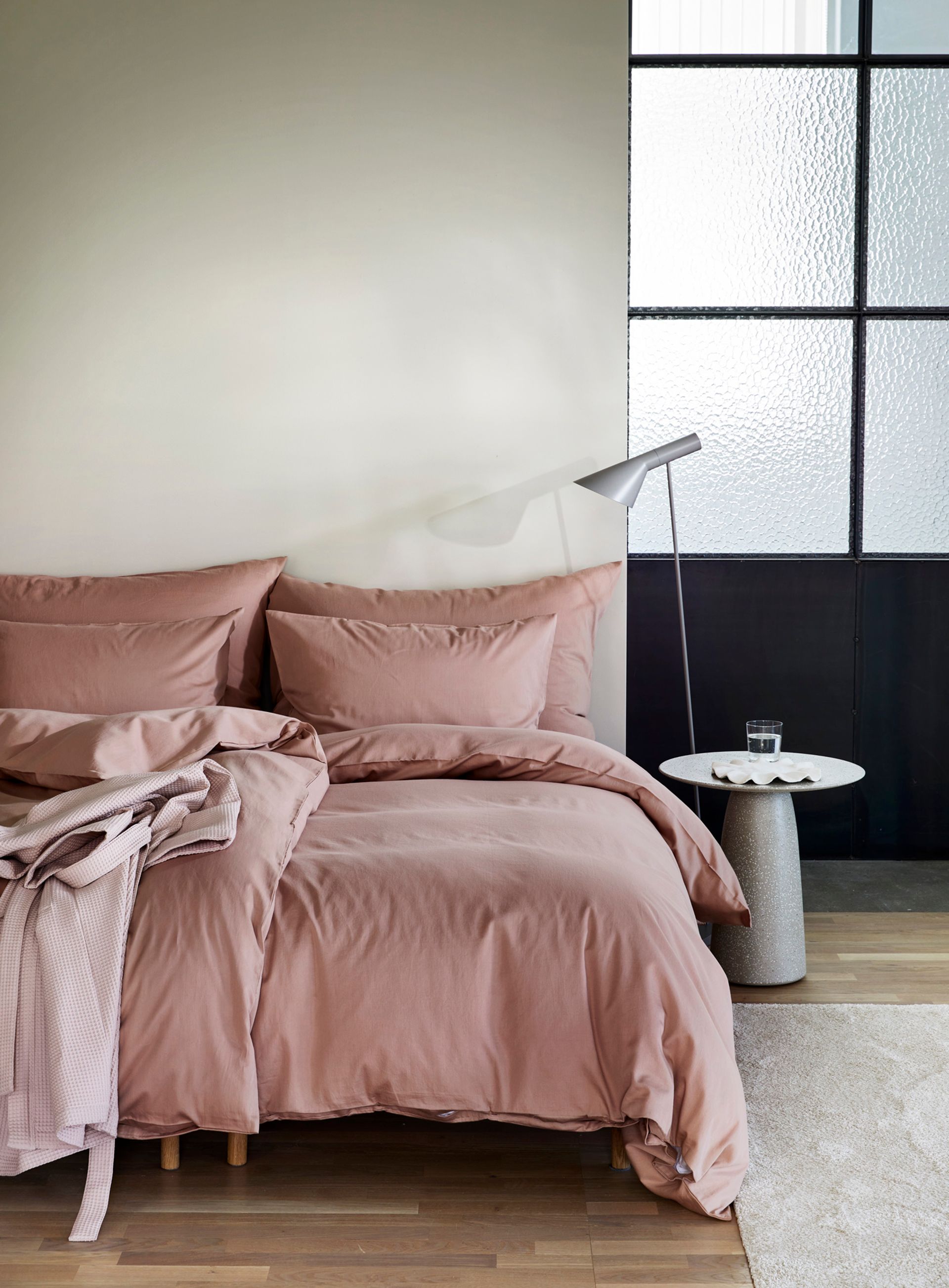 Nærbilde av oppredd seng med Høie Tor og Frøya sengesett i beige – en avslappet miks av smale striper og ensfarget bomull, som skaper en rolig og lun atmosfære på soverommet.