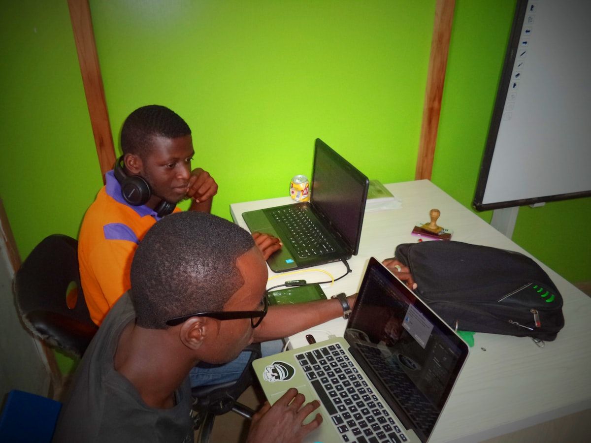 Two developers pair programming on laptops in a tech office