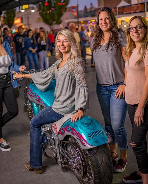 Woman sitting on motorcycle surrounded by friends at Street Vibrations.