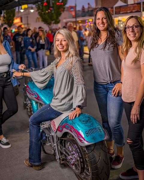 Woman sitting on motorcycle surrounded by friends at Street Vibrations.