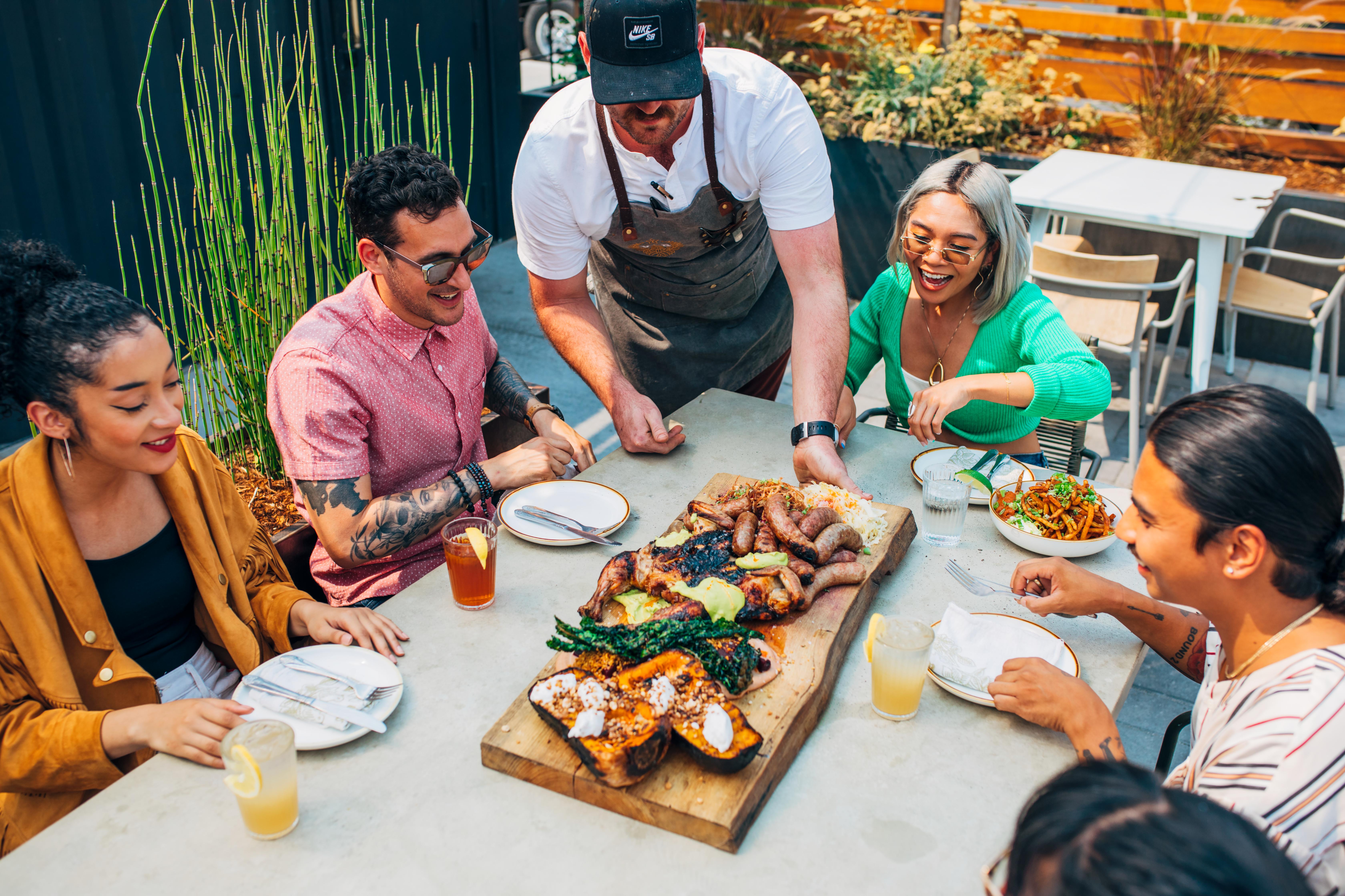 Group dining at a table with a board of different foods in the middle.