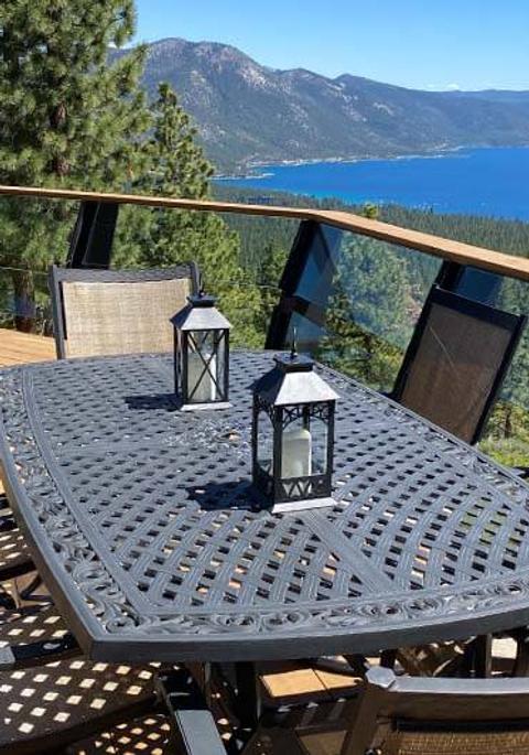 A patio table with chairs and lanterns overlooking a lake and mountains.