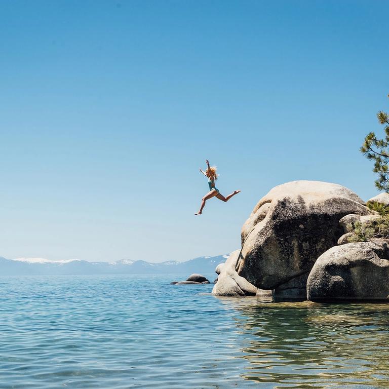 Girl jumping off rocks to swim in Lake Tahoe