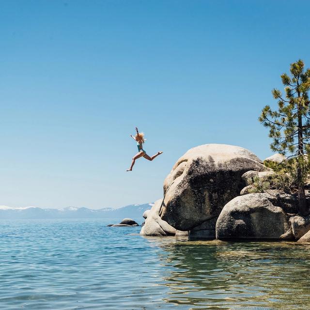Girl jumping off rocks to swim in Lake Tahoe