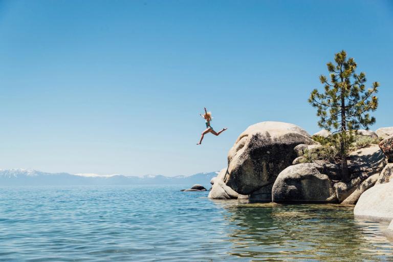 Girl jumping off rocks to swim in Lake Tahoe