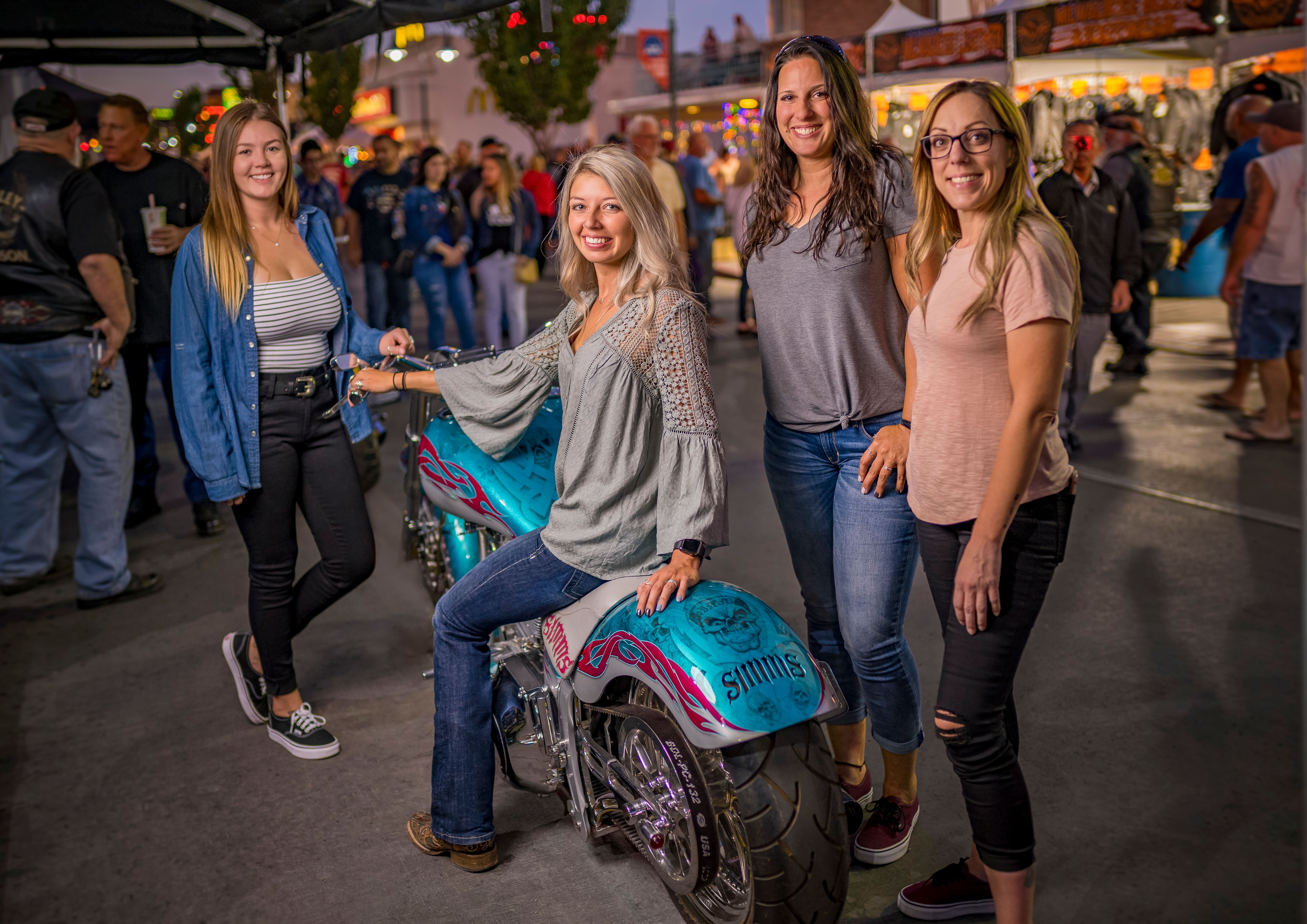 Woman sitting on motorcycle surrounded by friends at Street Vibrations.