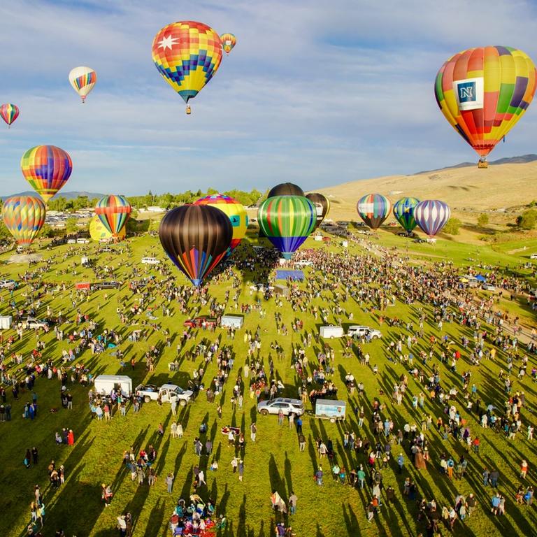 Hot air balloons in the sky over a field of spectators