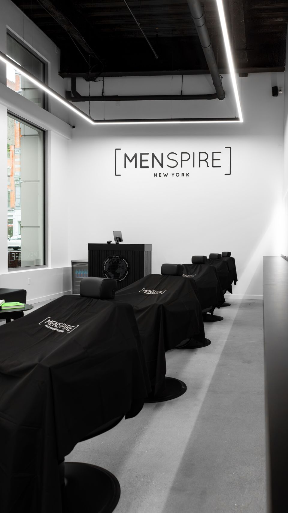 A row of black styling chairs under a long line of ceiling light at MENSPIRE New York