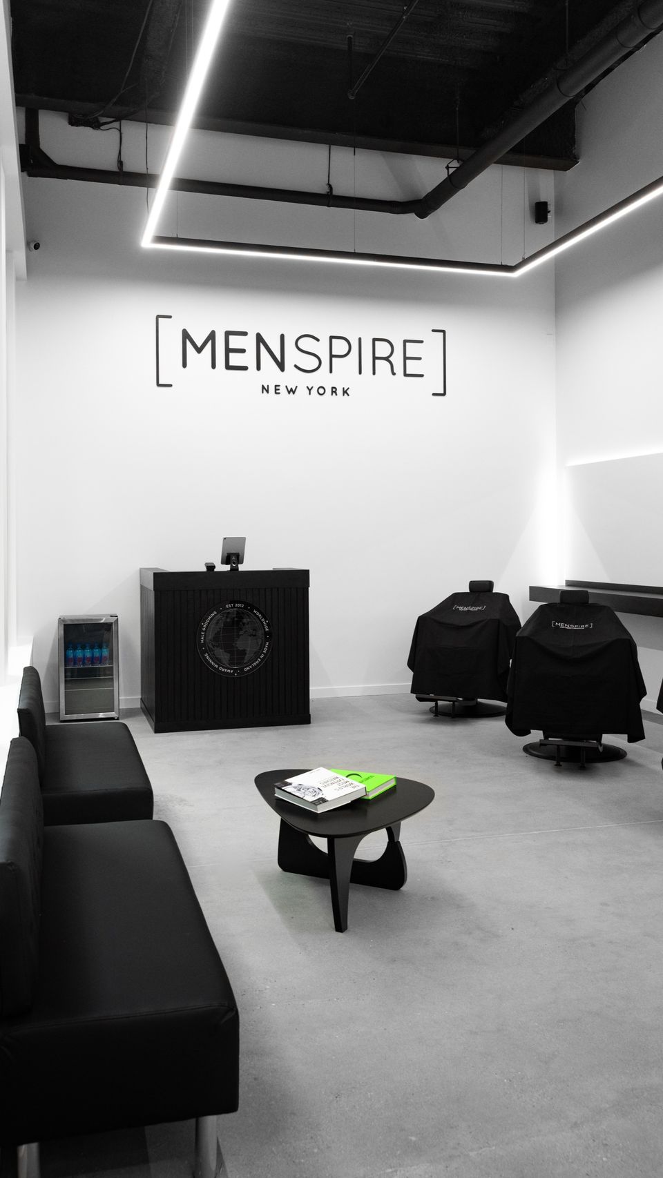 The waiting area at MENSPIRE New York with black sofas, a low table and styling chairs behind