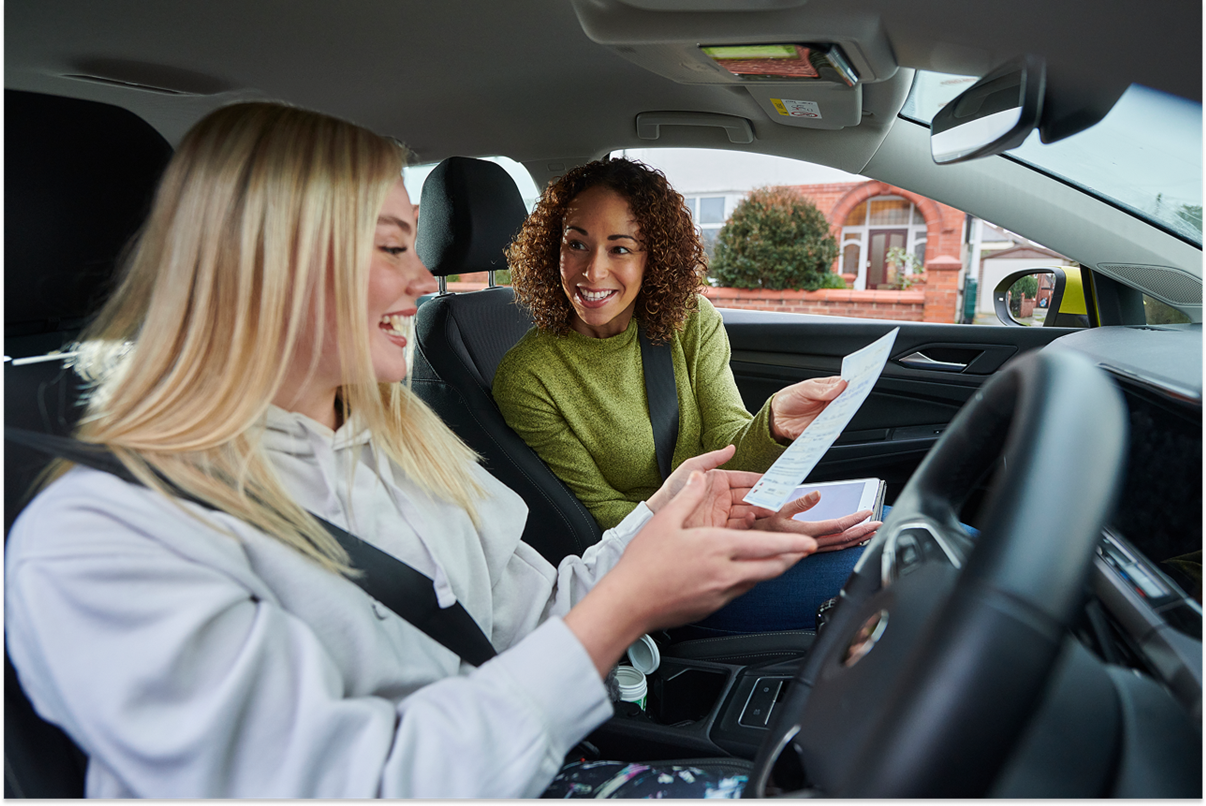 Young female driver and driving instructor holding driving test certificate