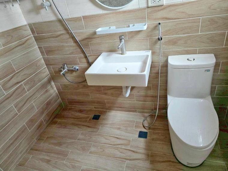 完工的浴室——洗手台、馬桶、蓮蓬頭、圓鏡到位，開放式無死角，木紋磚牆清新明亮。
