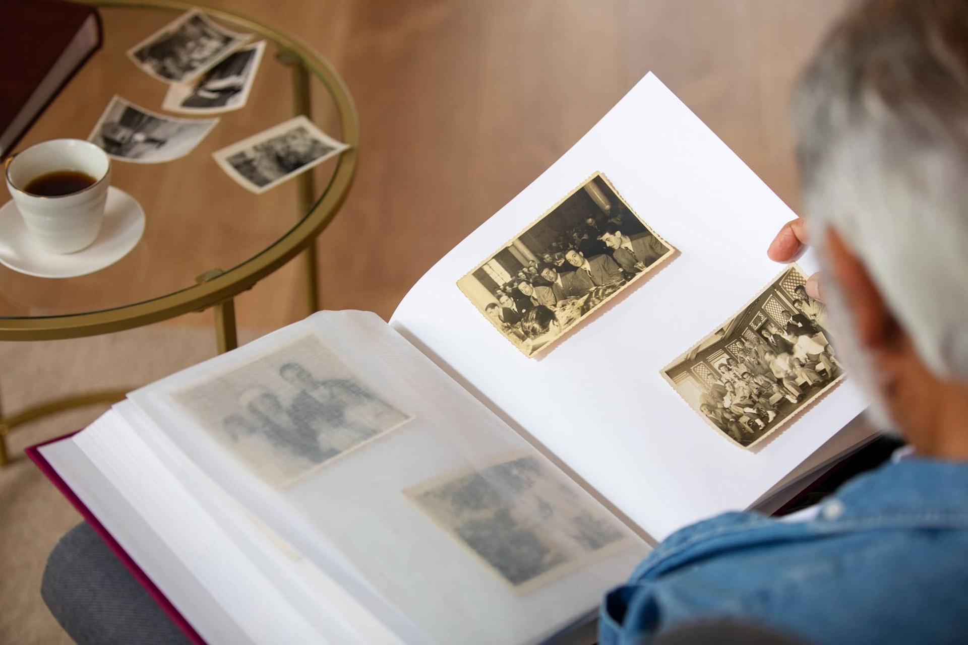 Mani che sfogliano un album di vecchie fotografie di famiglia in bianco e nero.