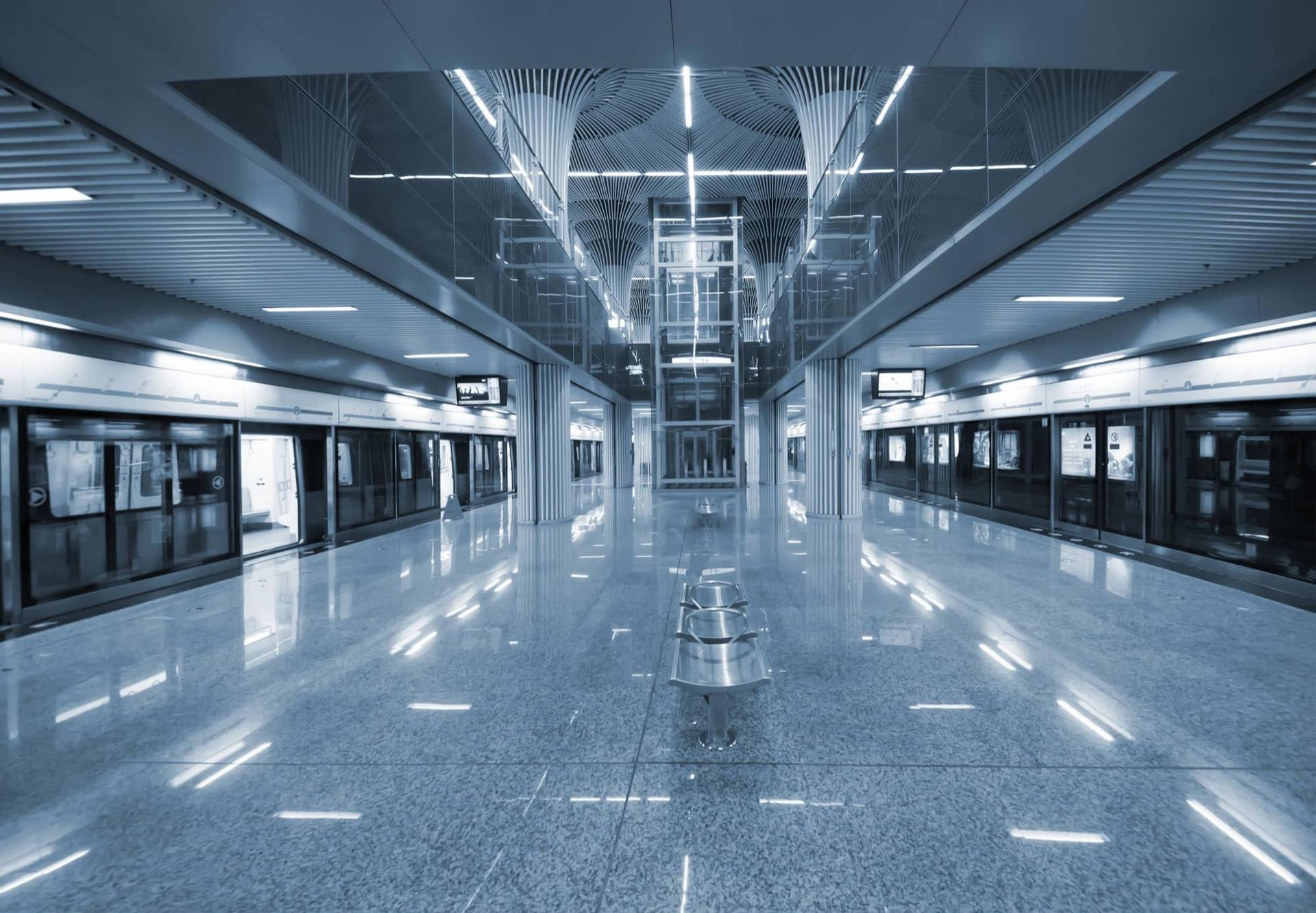 Empty metro station platform with blue-toned metallic walls and ceiling, train doors closed on both sides.