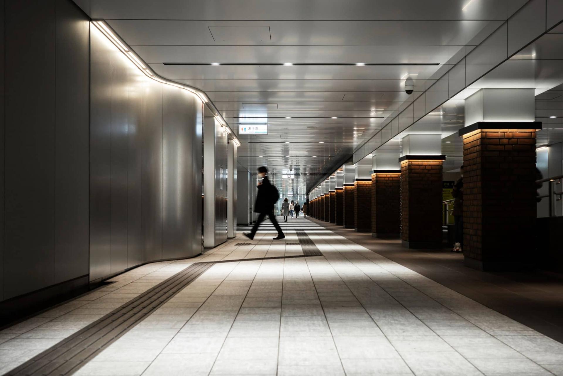 Una persona cammina in un sottopassaggio illuminato, con un leggero effetto di movimento.