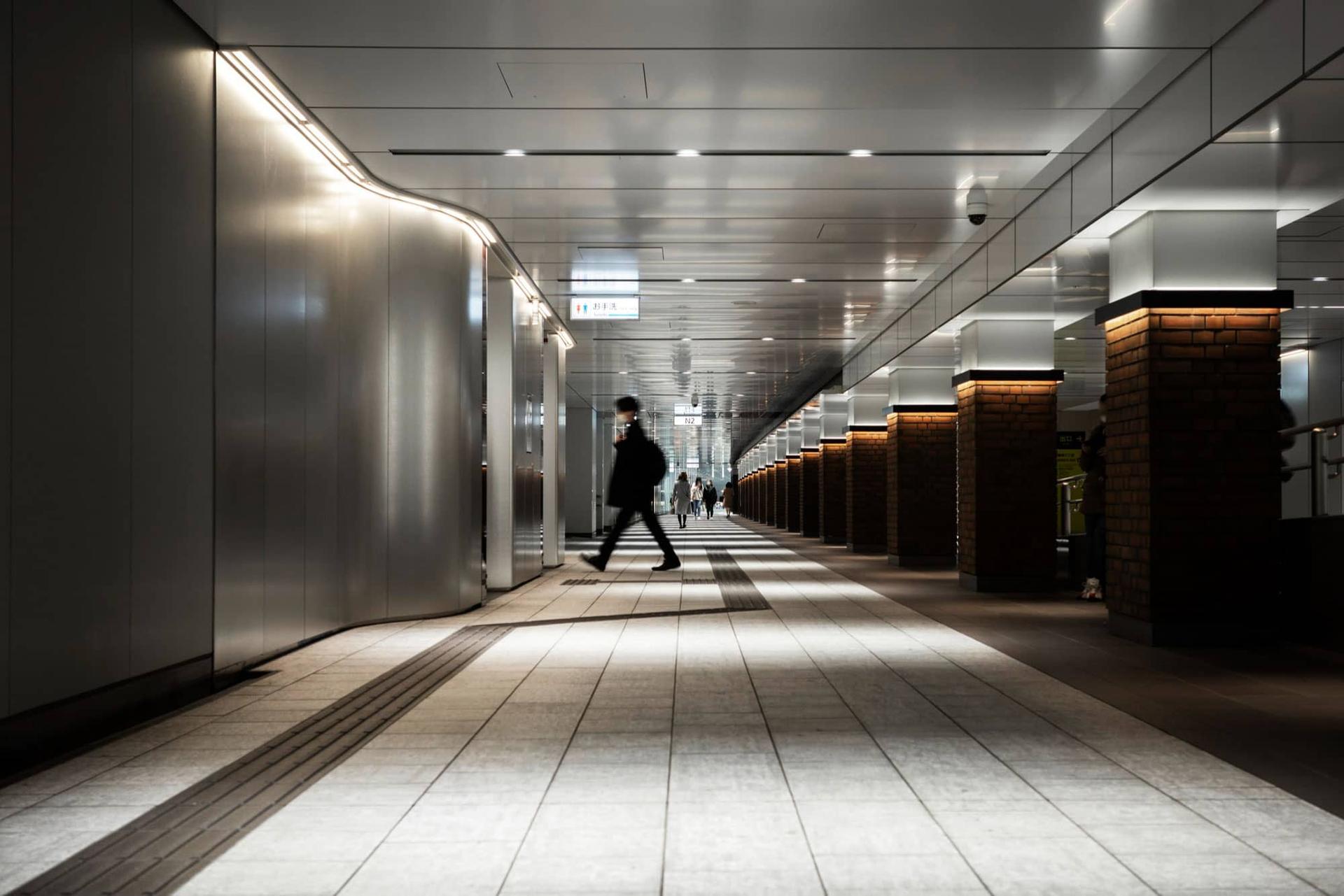Una persona cammina in un sottopassaggio illuminato, con un leggero effetto di movimento.