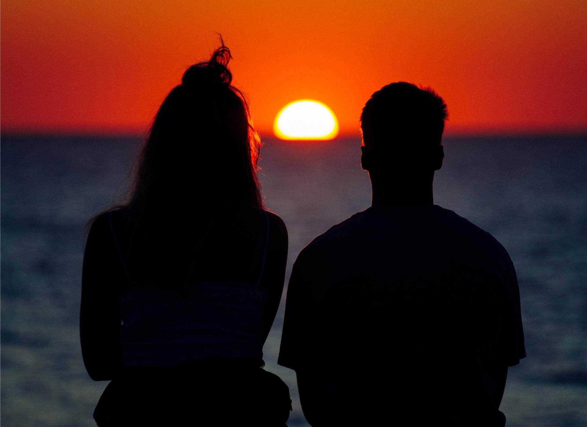 Due persone di spalle, sedute vicine ma senza toccarsi, che guardano il tramonto sul mare.