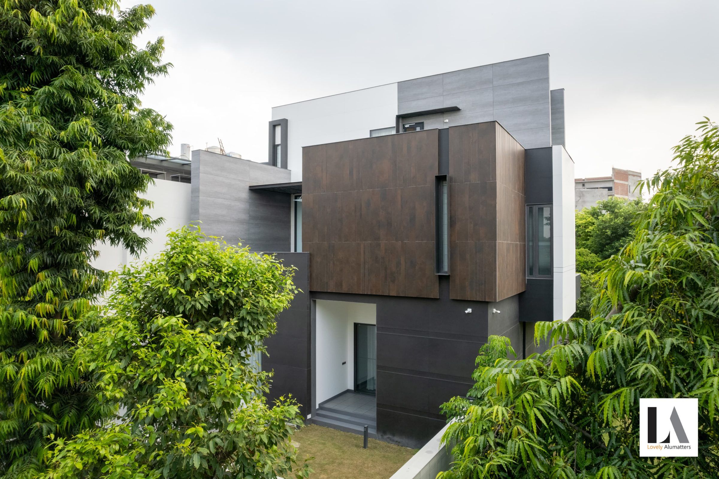 Bronze-clad volume with recessed windows seen through foliage